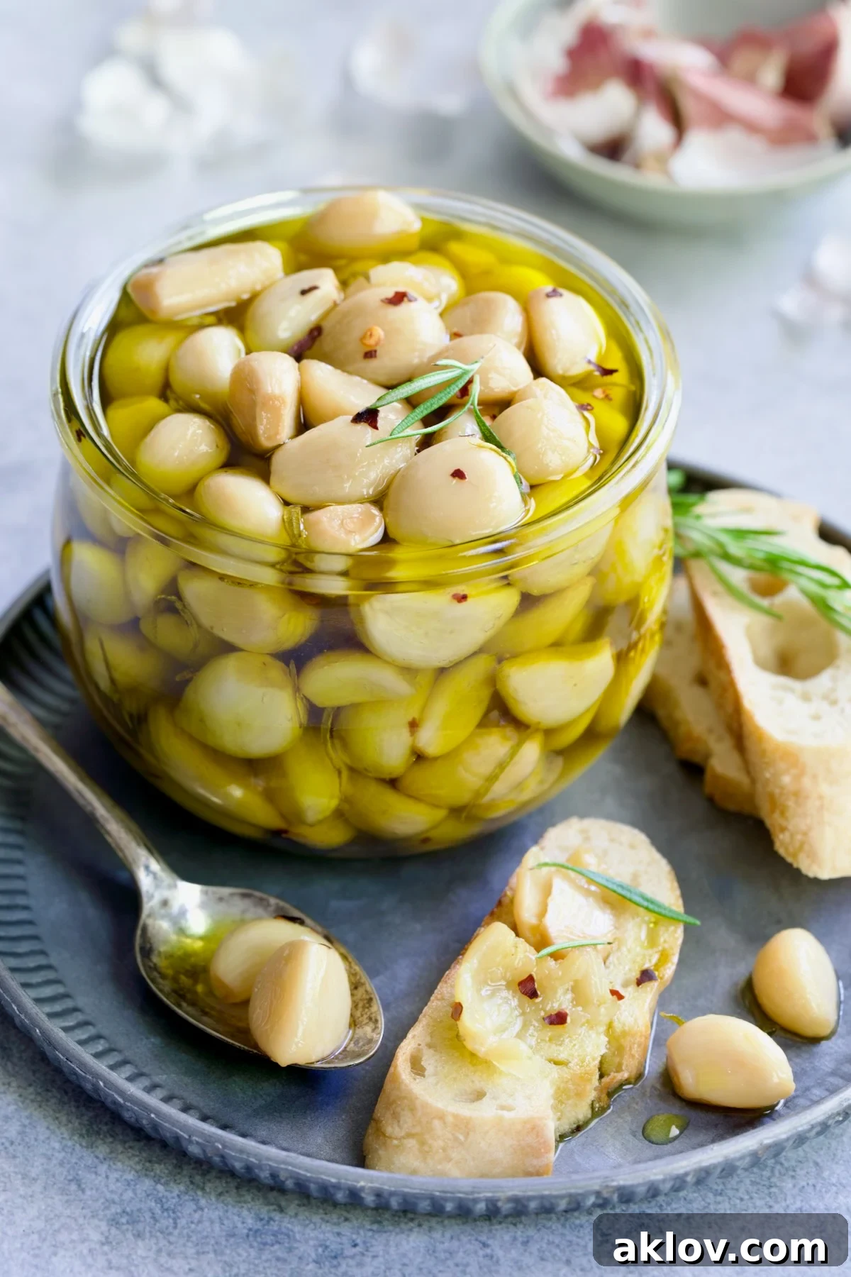 A glass jar brimming with homemade garlic confit, ready for use, with a spoonful of mashed confit on bread.