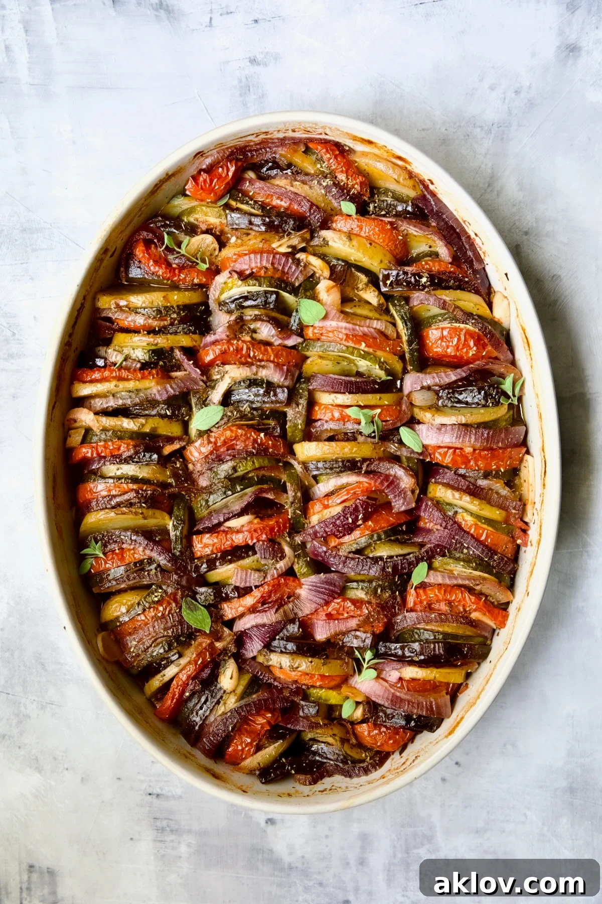 Briam (Greek Roast Vegetables) in oval white gratin dish with serving spoon.