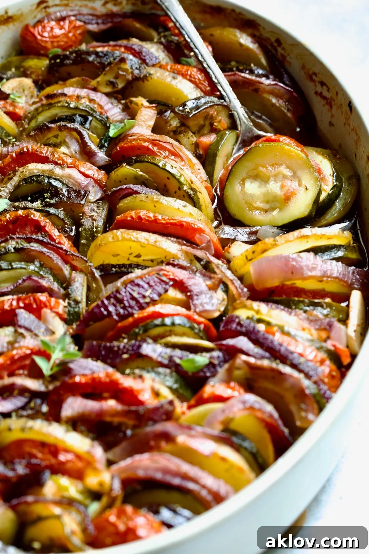 Briam (Greek Roast Vegetables) in oval white gratin dish with serving spoon.