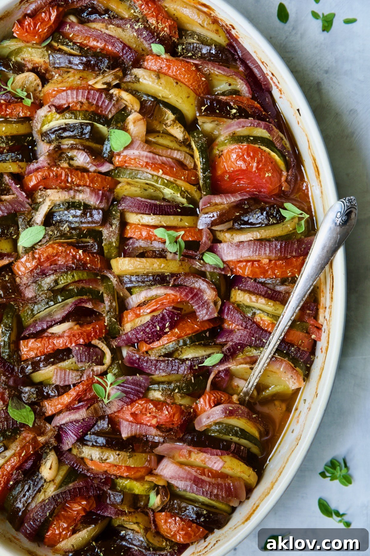 Briam (Greek Roast Vegetables) in oval white gratin dish with serving spoon.