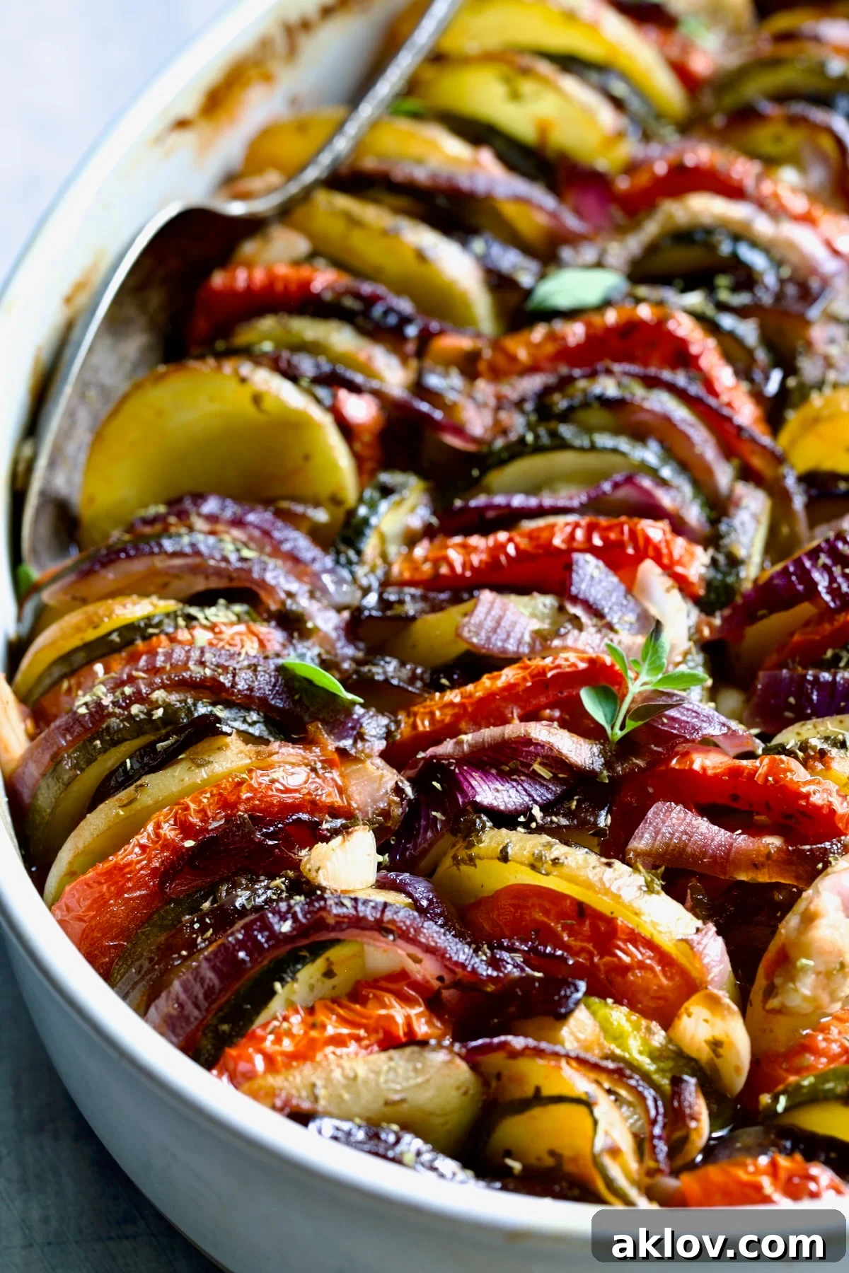 Briam (Greek Roast Vegetables) in oval white gratin dish with serving spoon.