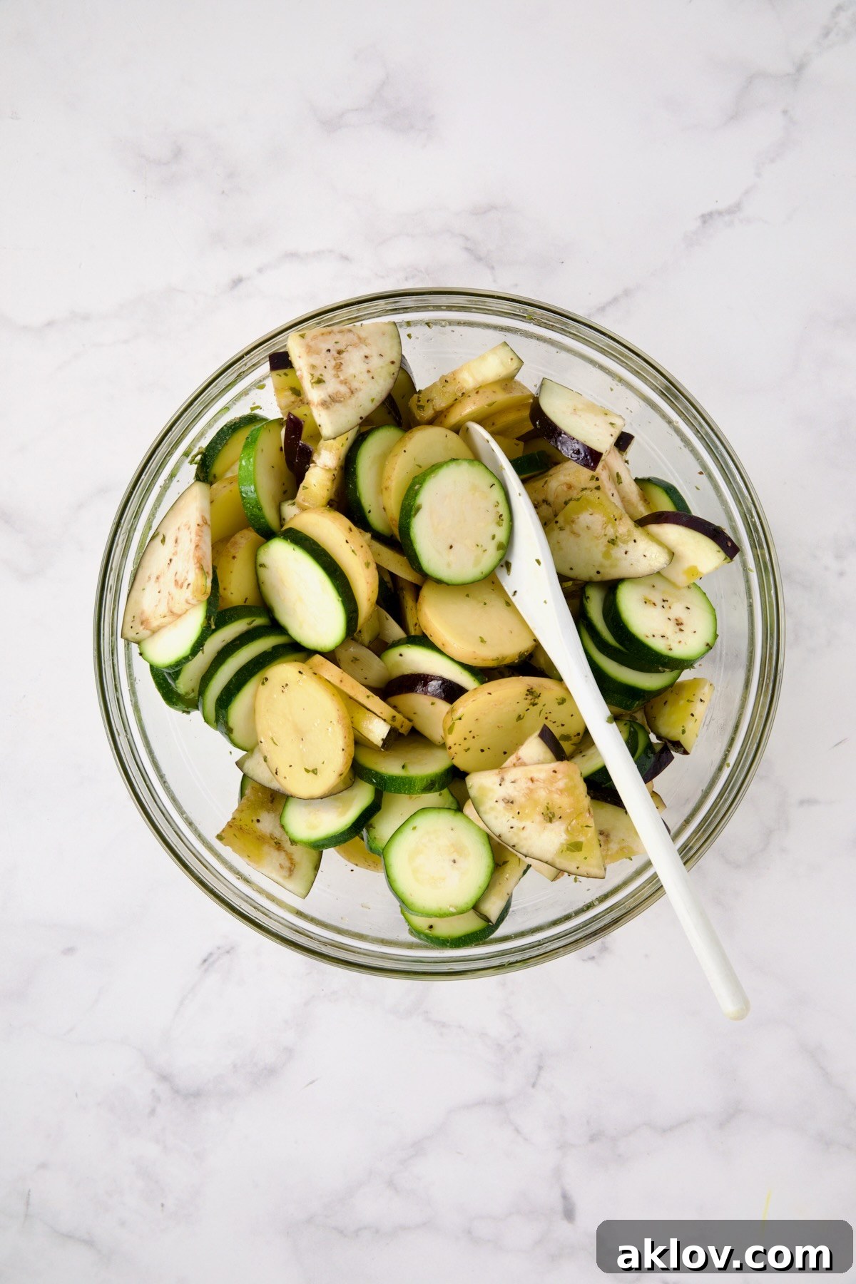 Zucchini, potatoes and eggplant being tossed with flavored olive oil and dried oregano.