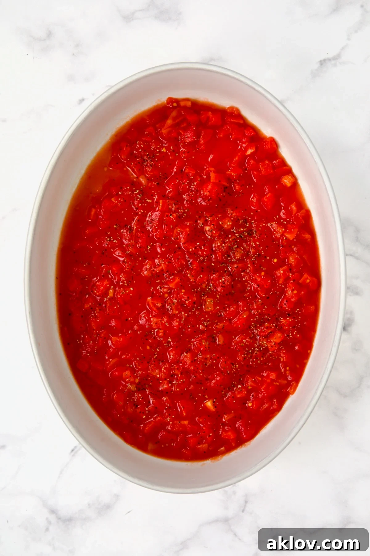 Petite diced tomatoes spread over the bottom of an oval white baking dish.