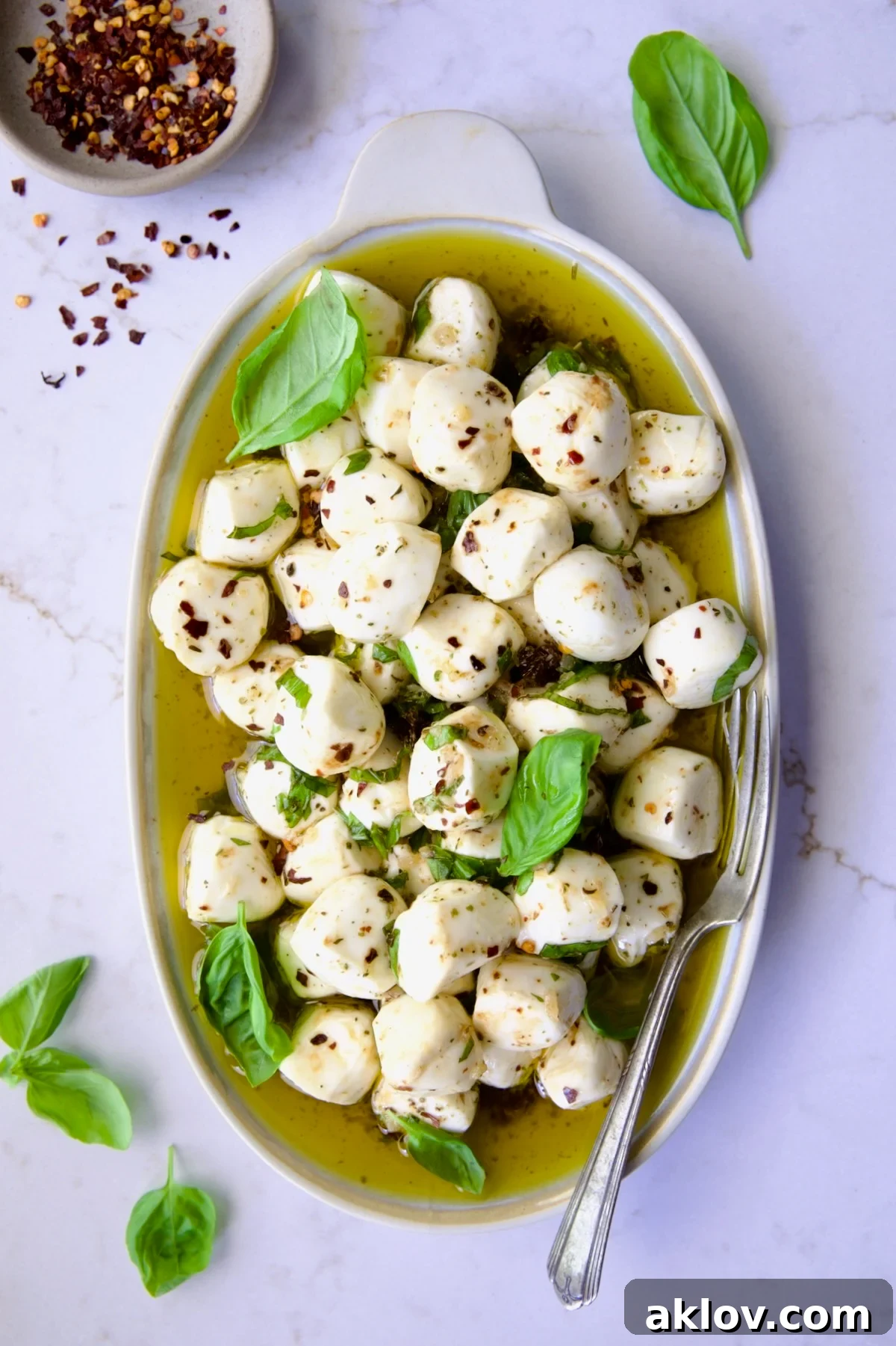 Marinated Mozzarella Balls on oval platter garnished with fresh basil leaves.