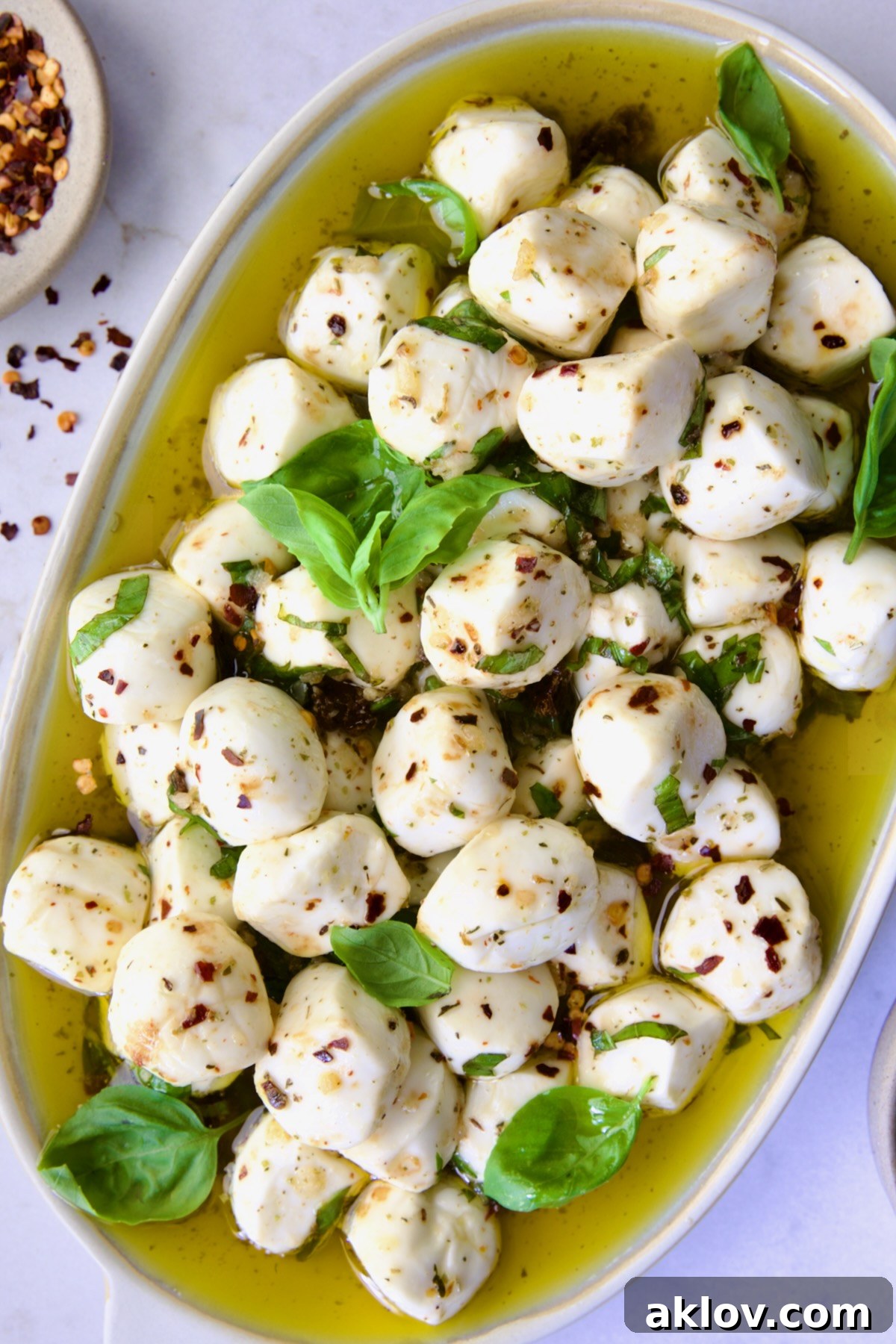 Marinated Mozzarella Balls on oval platter garnished with fresh basil leaves.