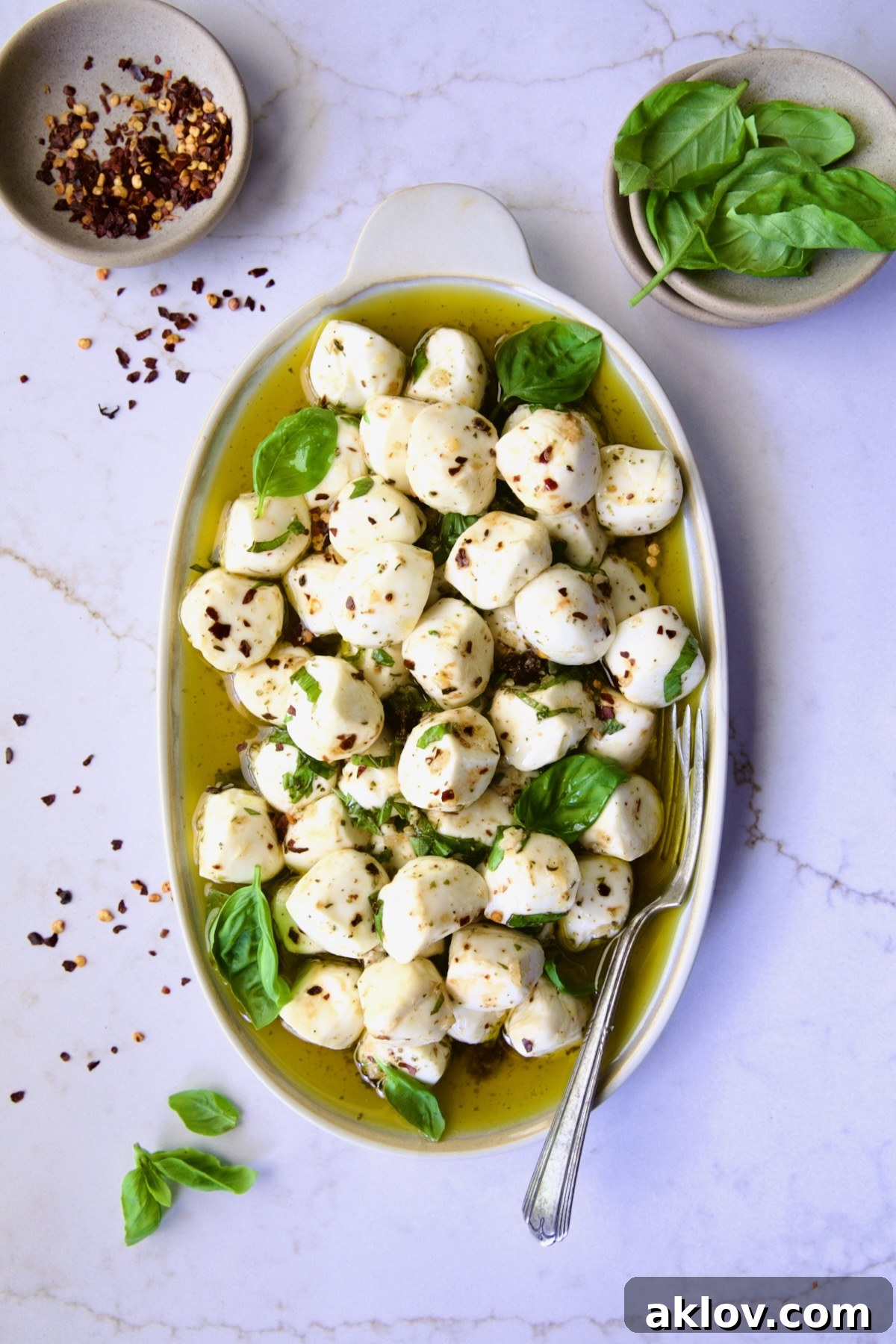 Marinated Mozzarella Balls on oval platter garnished with fresh basil leaves.