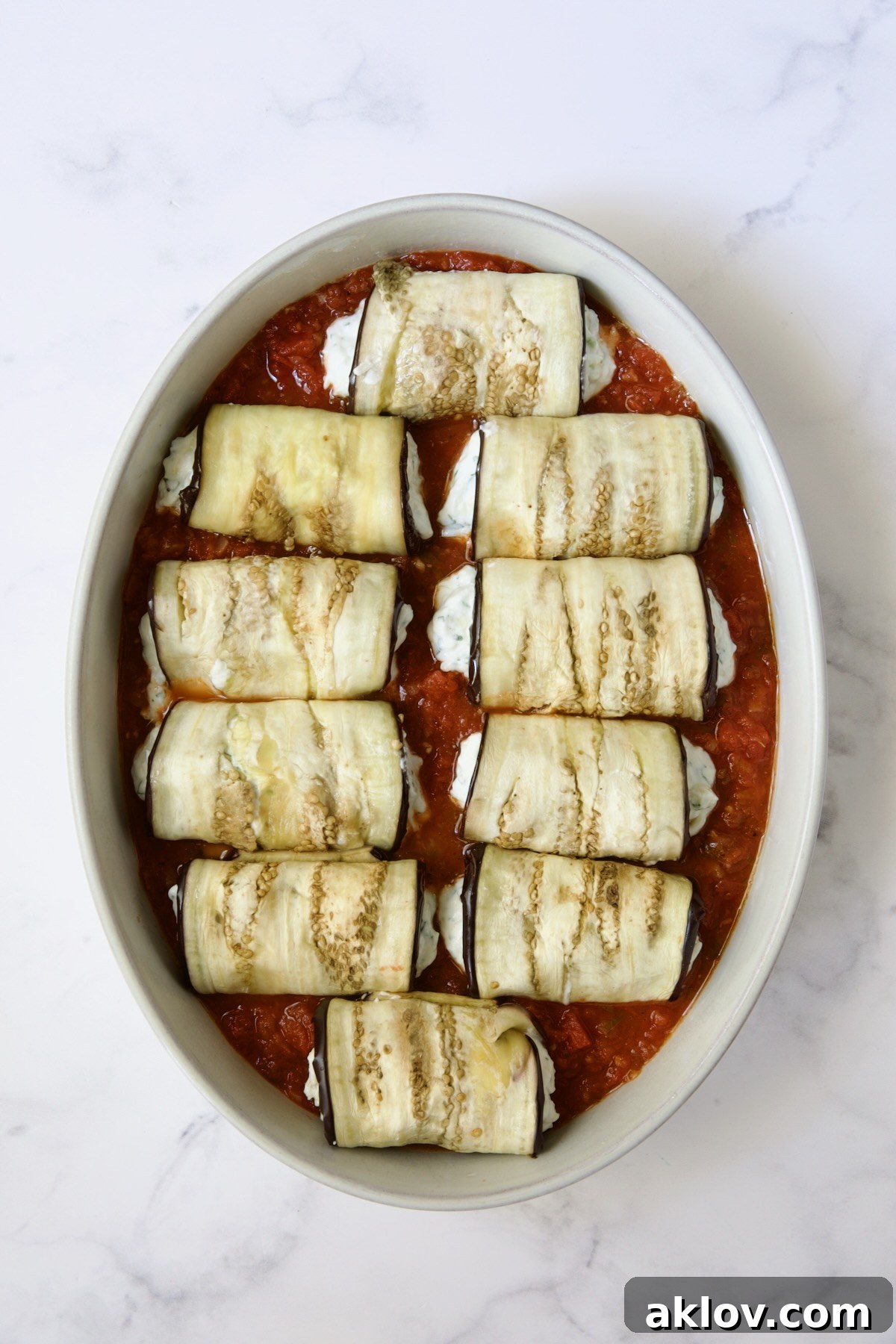 Ten eggplant slices placed on tomato sauce in oval baking dish.