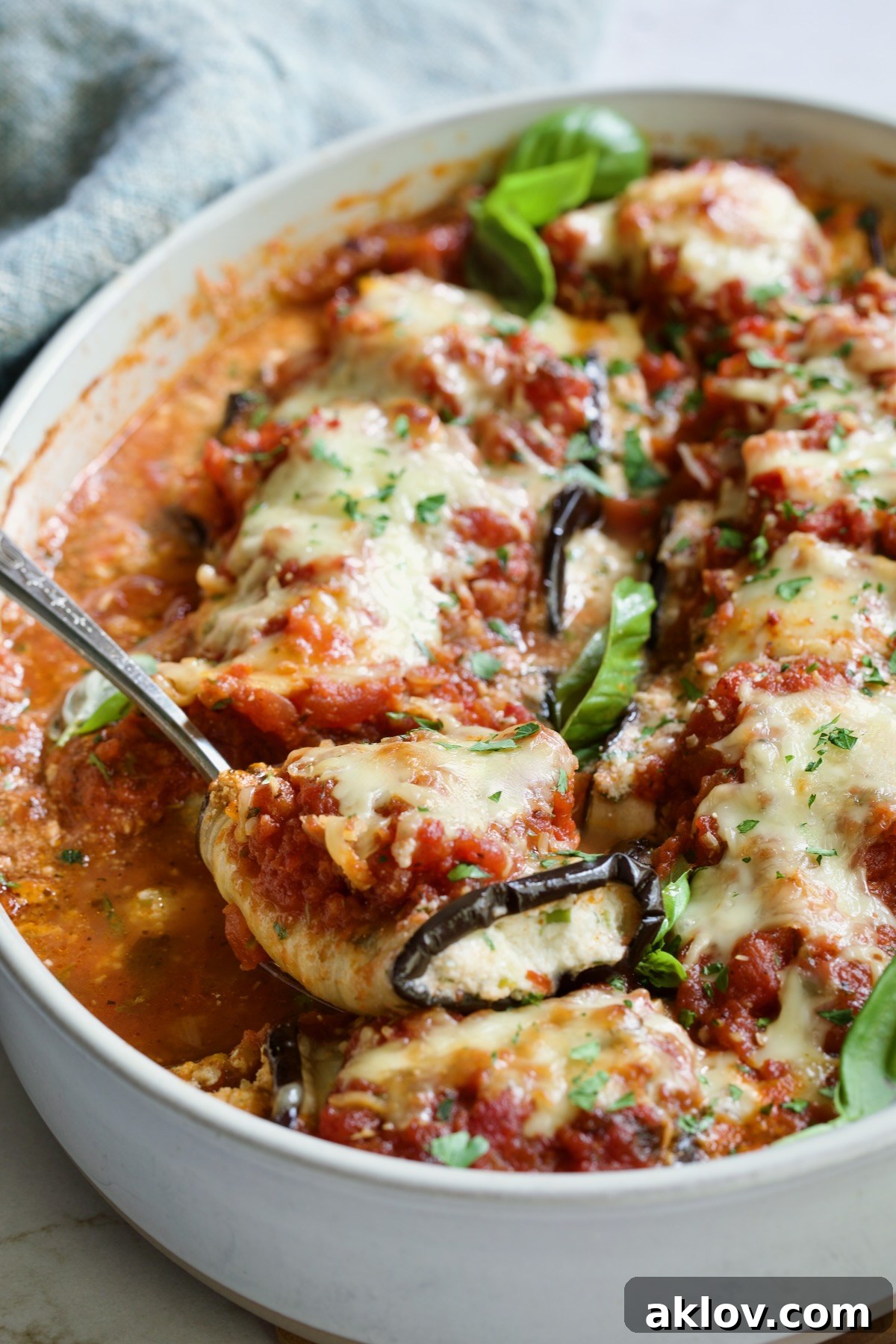 Serving spoon scooping one Eggplant Rollatini from oval baking dish.