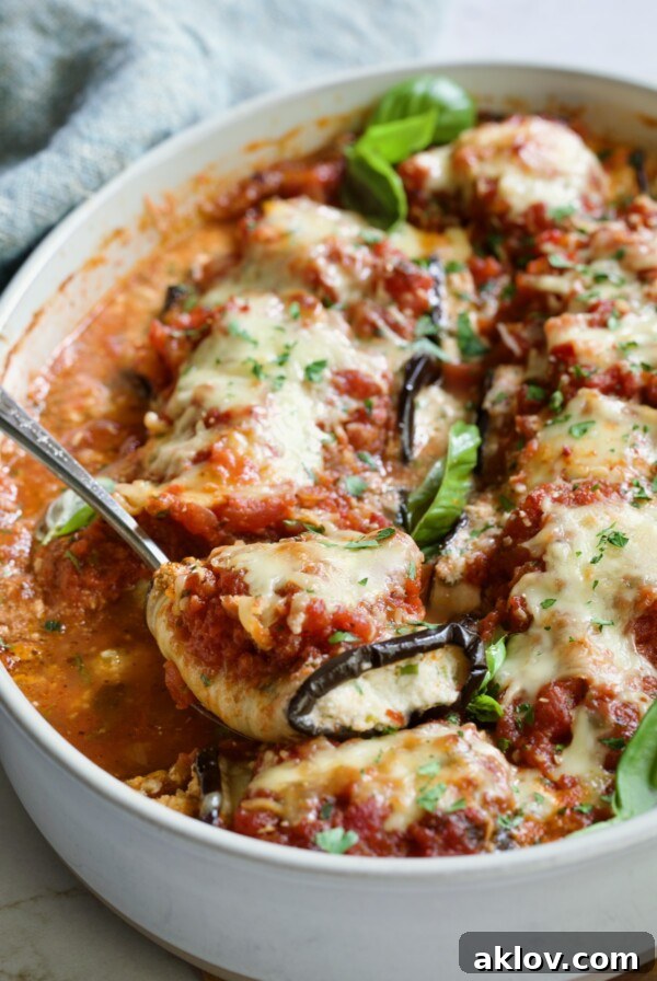 Serving spoon scooping one Eggplant Rollatini from oval baking dish.
