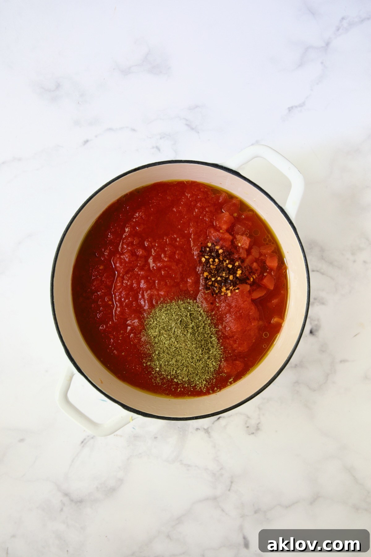 Crushed tomatoes, diced tomatoes, Italian seasoning and crushed red pepper flakes in white Dutch oven.