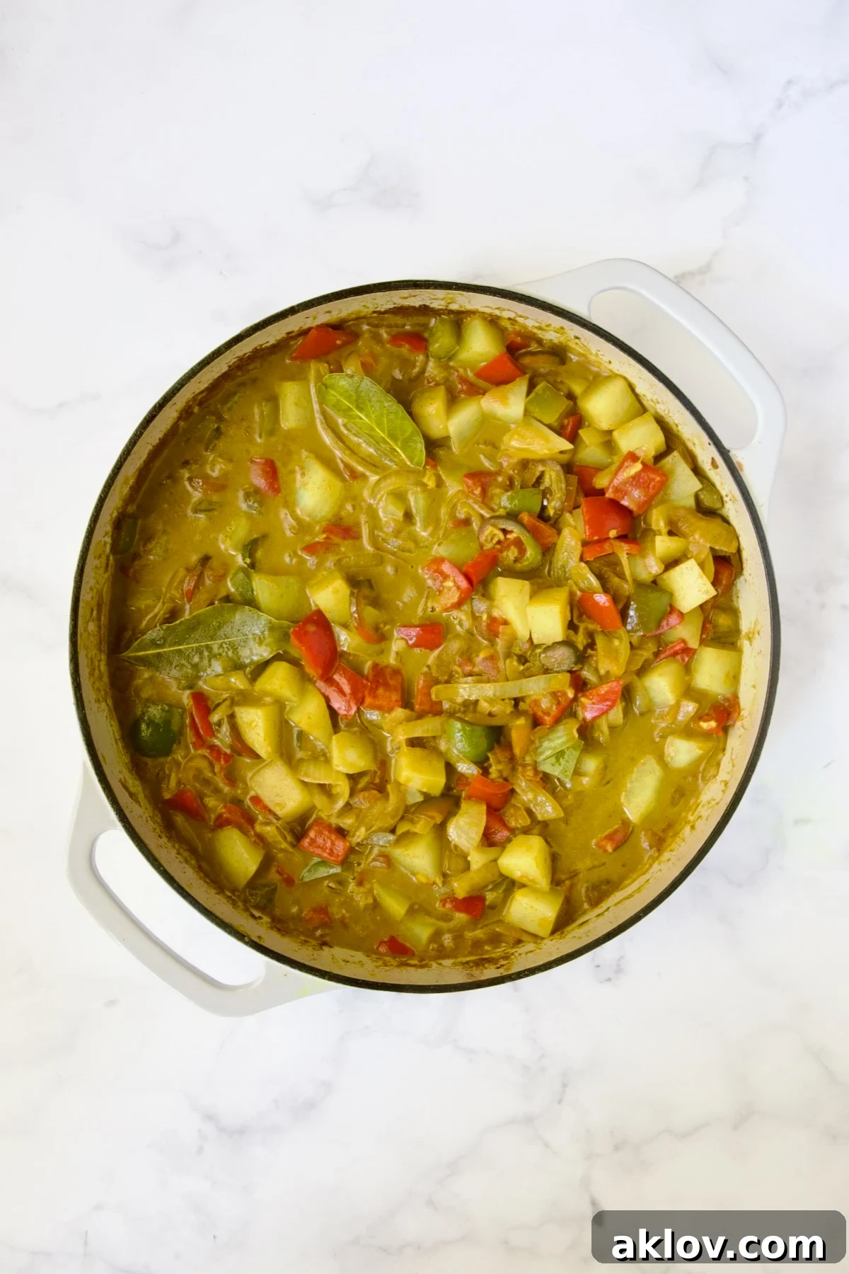 Comforting Chicken Potato Curry 11 Tender, cooked potatoes, peppers, and onions simmering in a rich, flavorful sauce in a white enamel cast iron skillet.