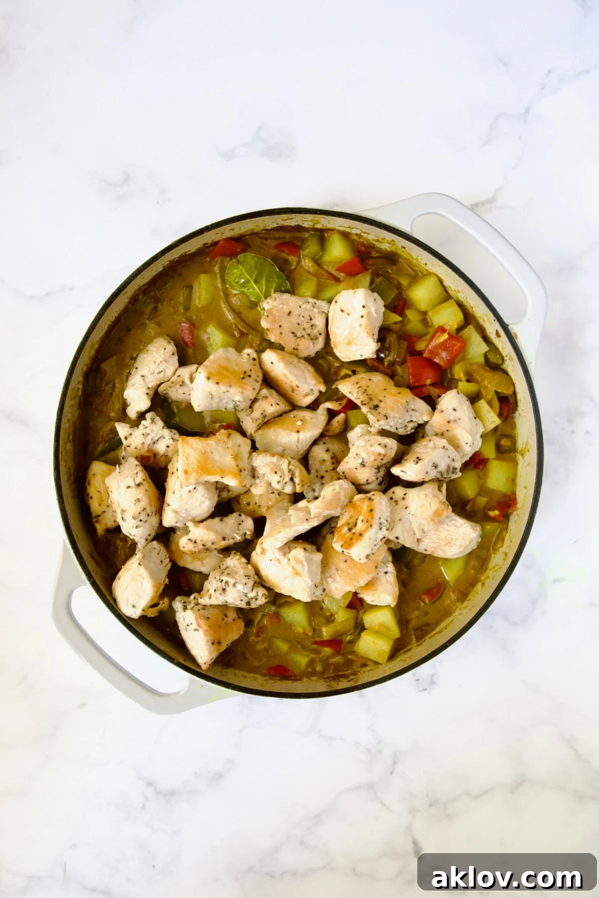 Comforting Chicken Potato Curry 12 The browned chicken pieces are carefully added back to the simmering curry in a white enamel cast iron skillet, ready to finish cooking.