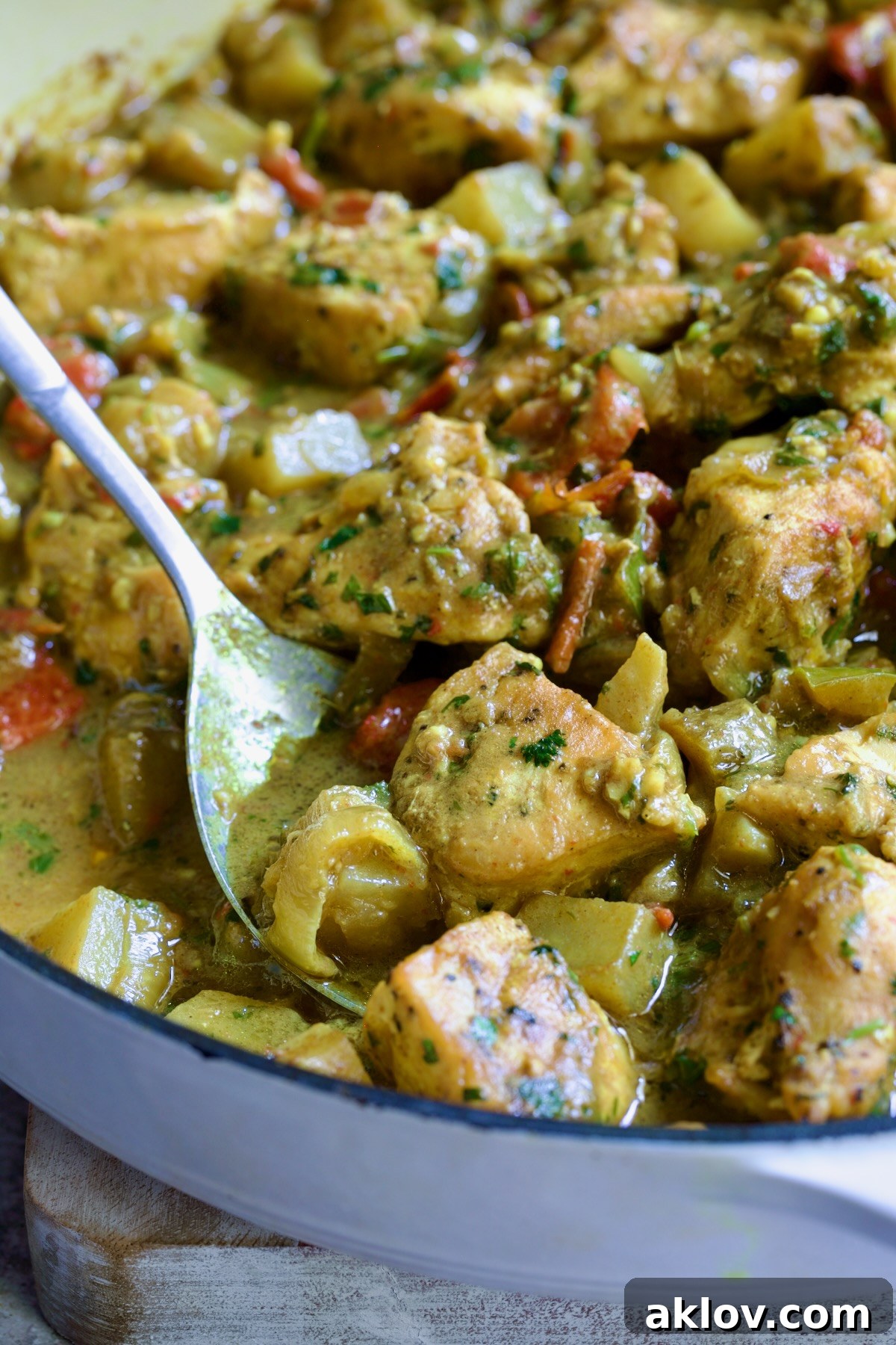 Spoon scooping out some Chicken and Potato Curry from white enamel cast iron skillet.