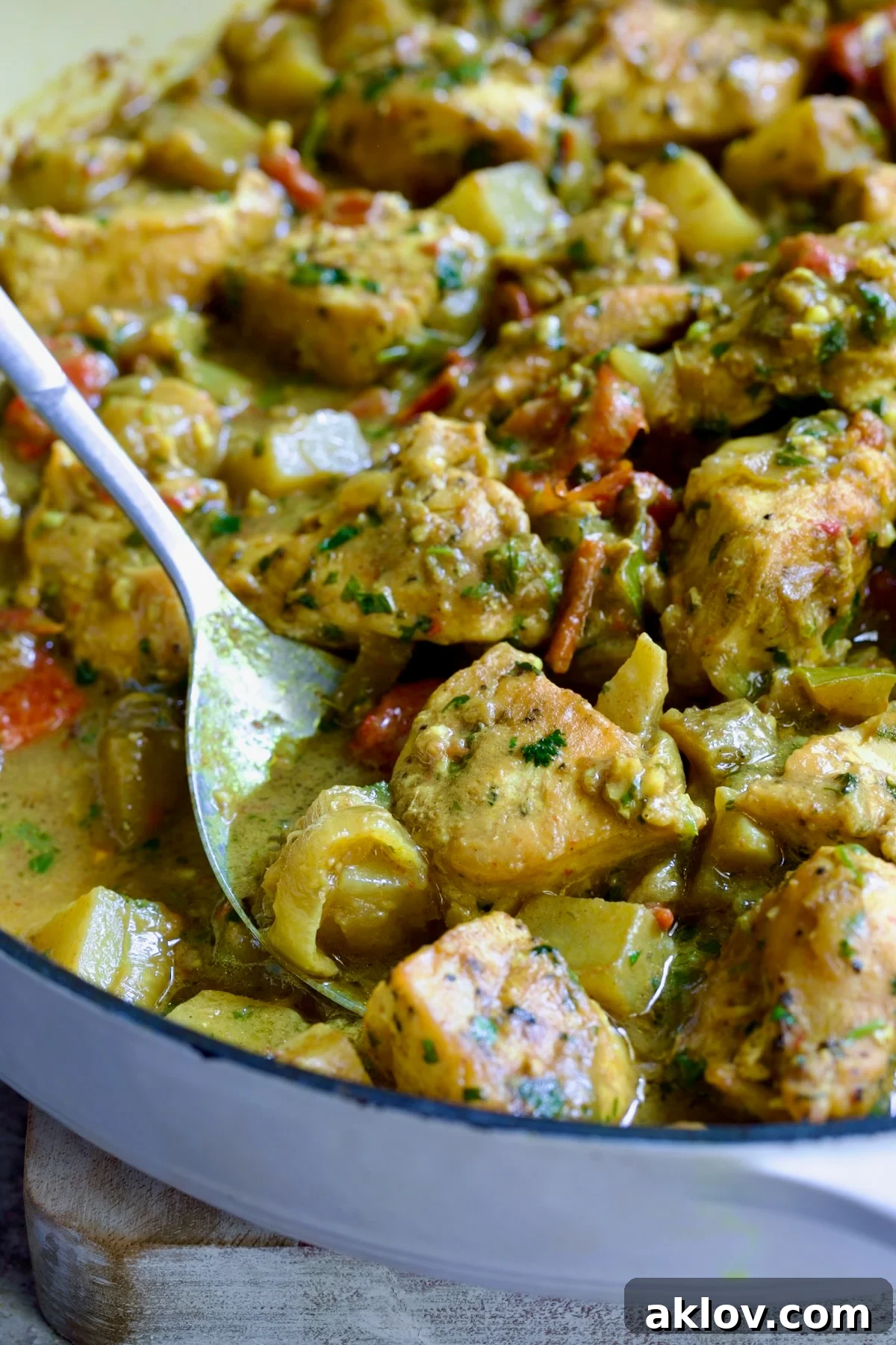 Comforting Chicken Potato Curry 16 A serving spoon expertly scooping out a generous portion of the rich and flavorful Chicken and Potato Curry from a white enamel cast iron skillet.
