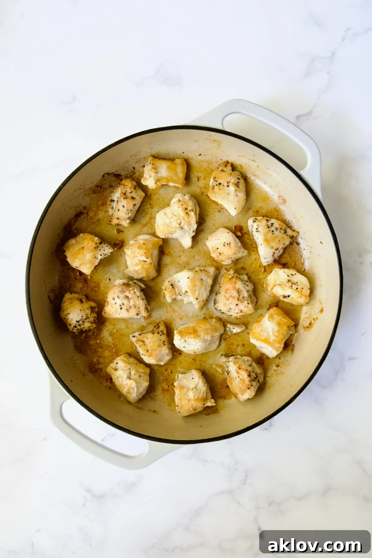 Browned cubed chicken in white enamel cast iron skillet.