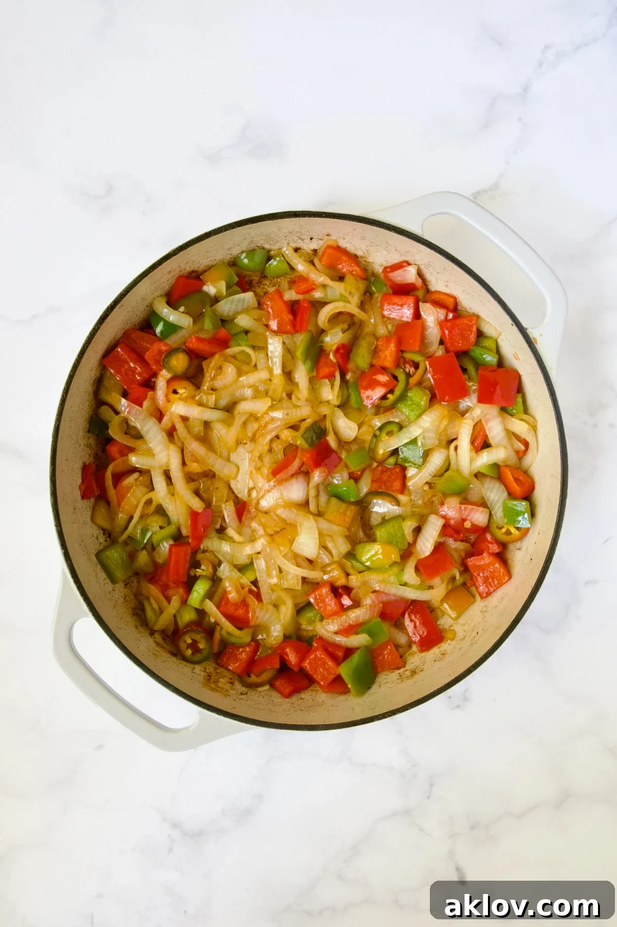 Comforting Chicken Potato Curry 7 A colorful medley of cooked onions, red bell pepper, green bell pepper, and jalapenos simmering in a white enamel cast iron skillet.
