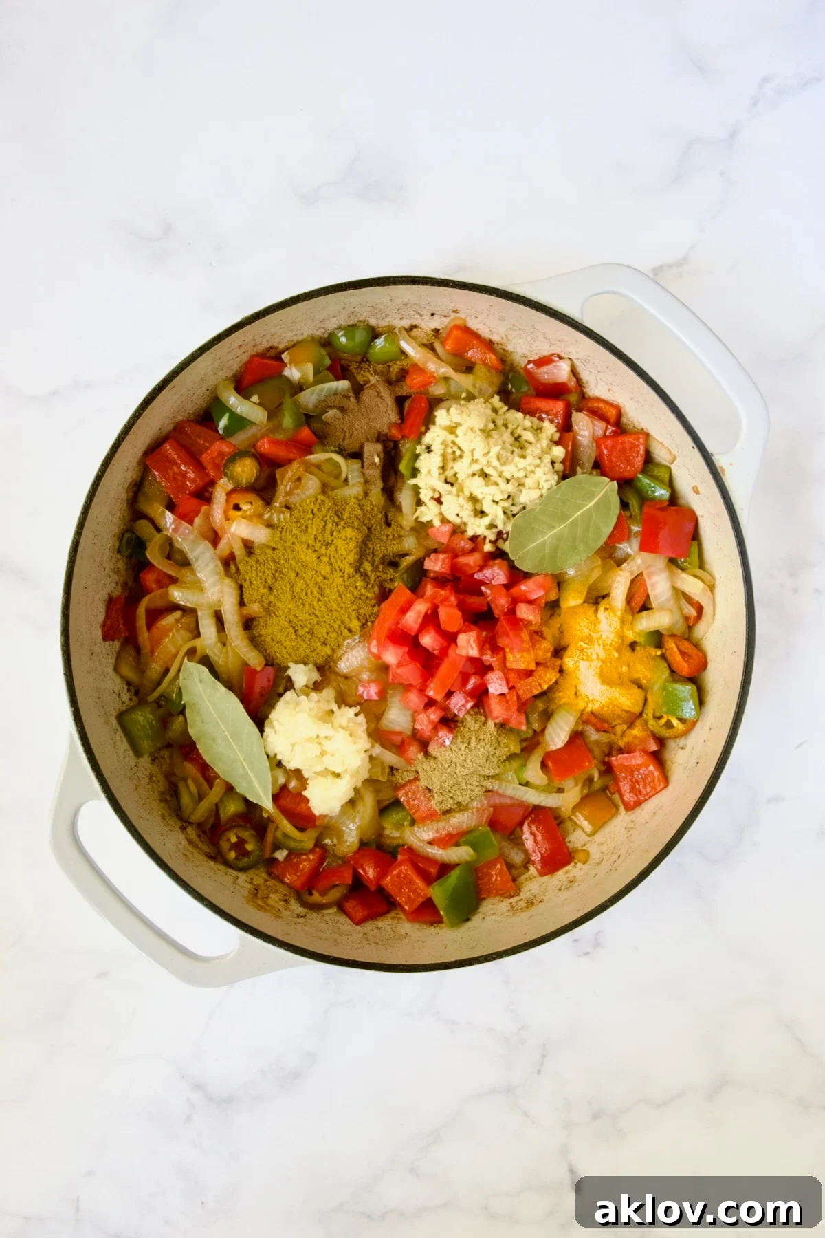 Comforting Chicken Potato Curry 8 The aromatic blend of cooked onions and peppers awaiting the introduction of rich spices, poised to be mixed in a white enamel cast iron skillet.