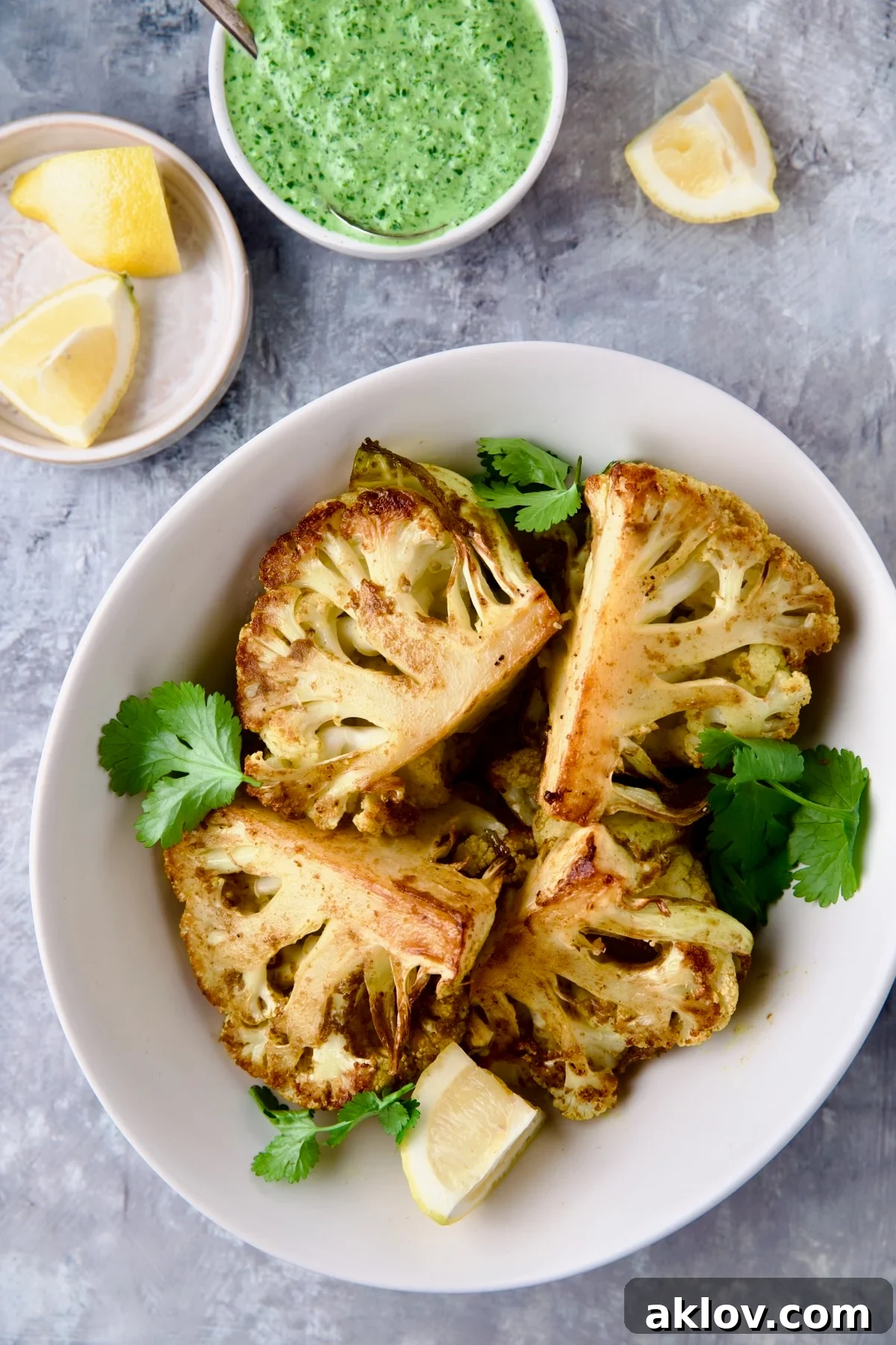 Four wedges of Curry Roasted Cauliflower Wedges with Cilantro Chutney in white bowl with lemon wedges.
