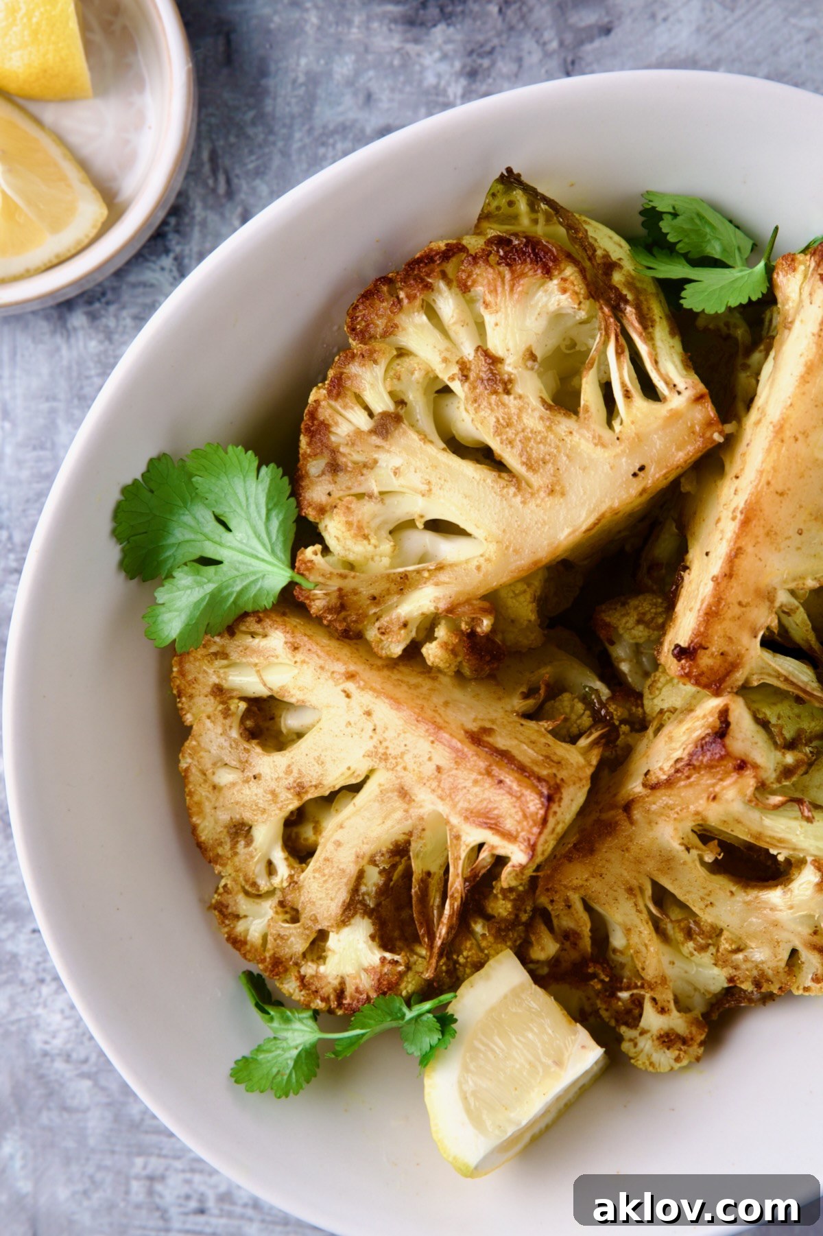 Wedges of Curry Roasted Cauliflower in white oval bowl with lemon wedges.