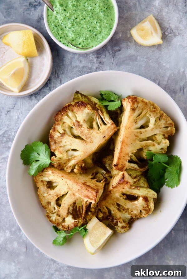 Four wedges of Curry Roasted Cauliflower Wedges with Cilantro Chutney in white bowl with lemon wedges.