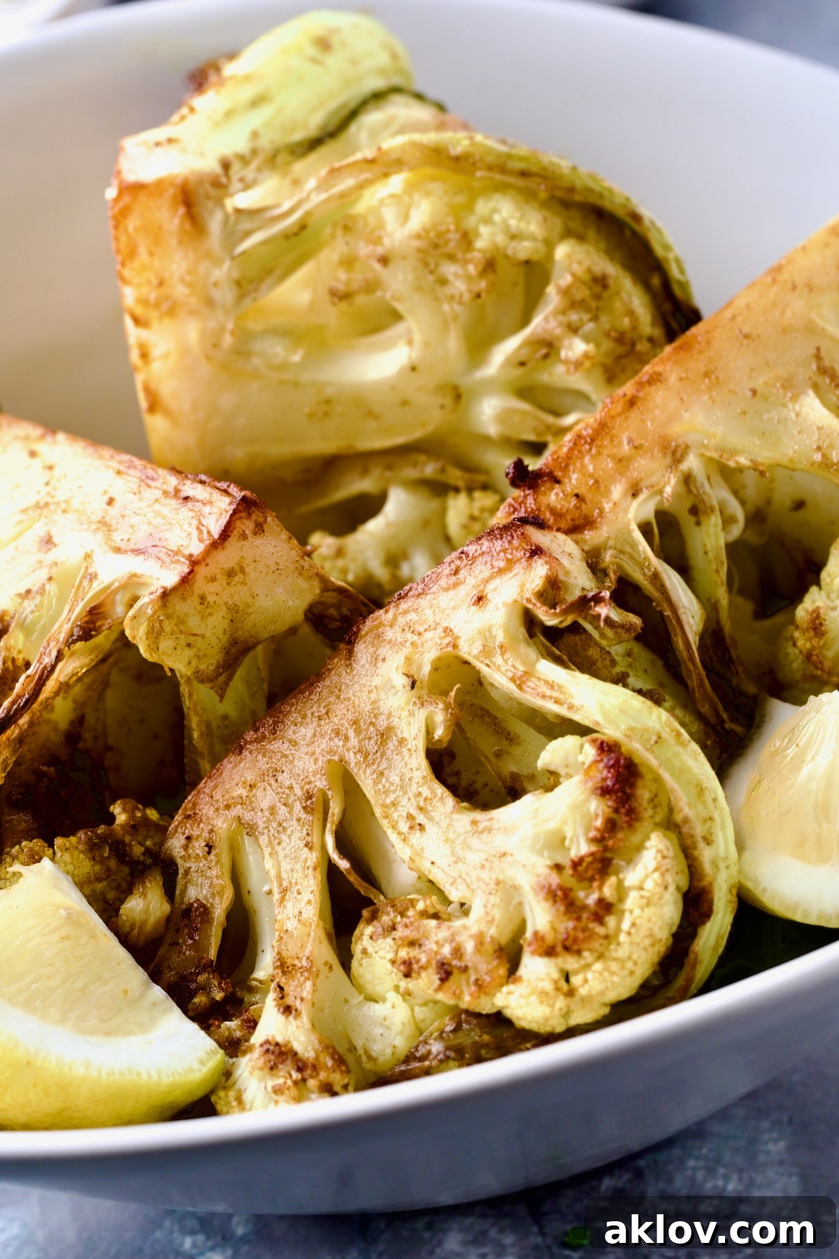 Curry Roasted Cauliflower Wedges in white bowl with lemon wedge.