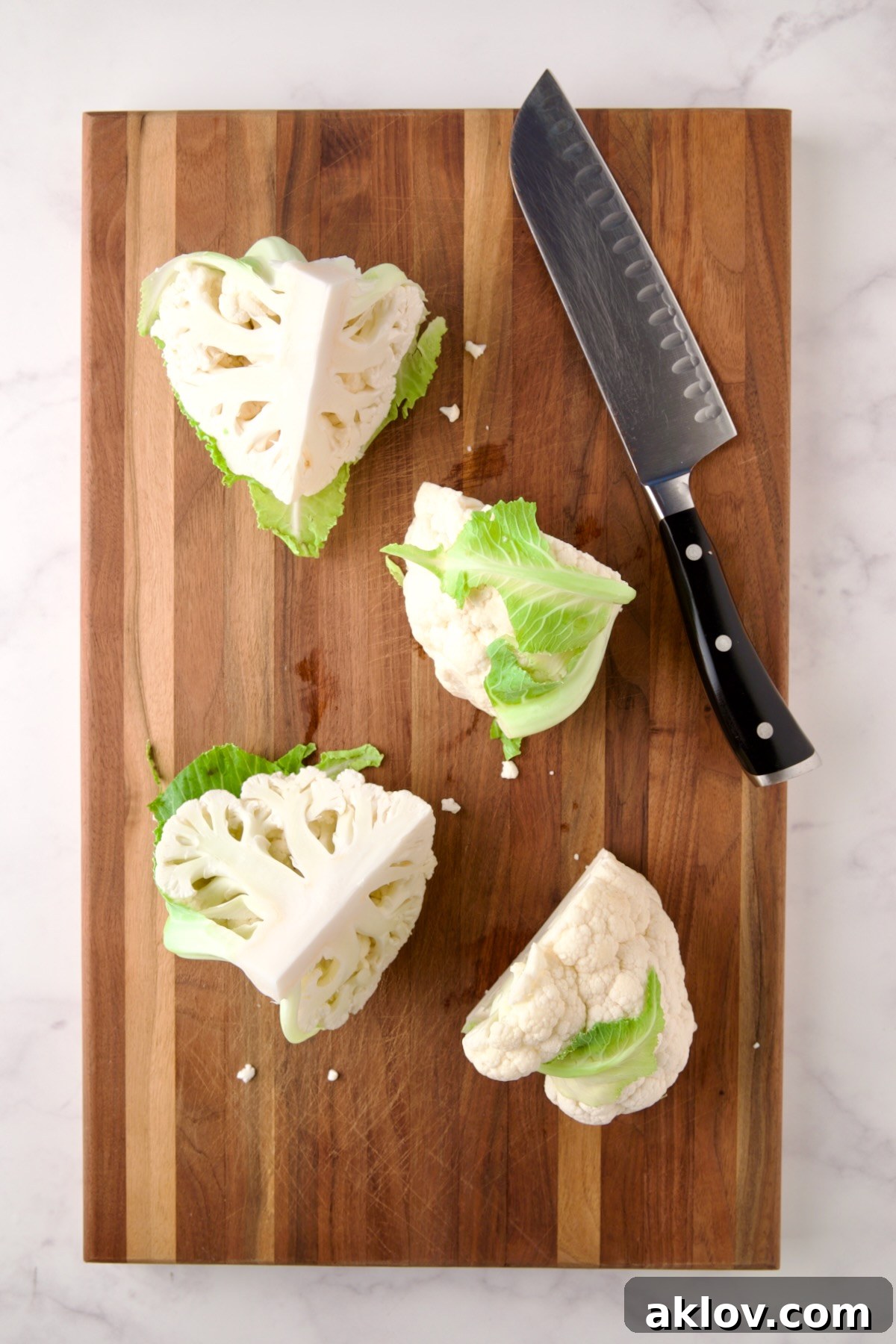 Four wedges of cauliflower on wood cutting board with chef's knife.