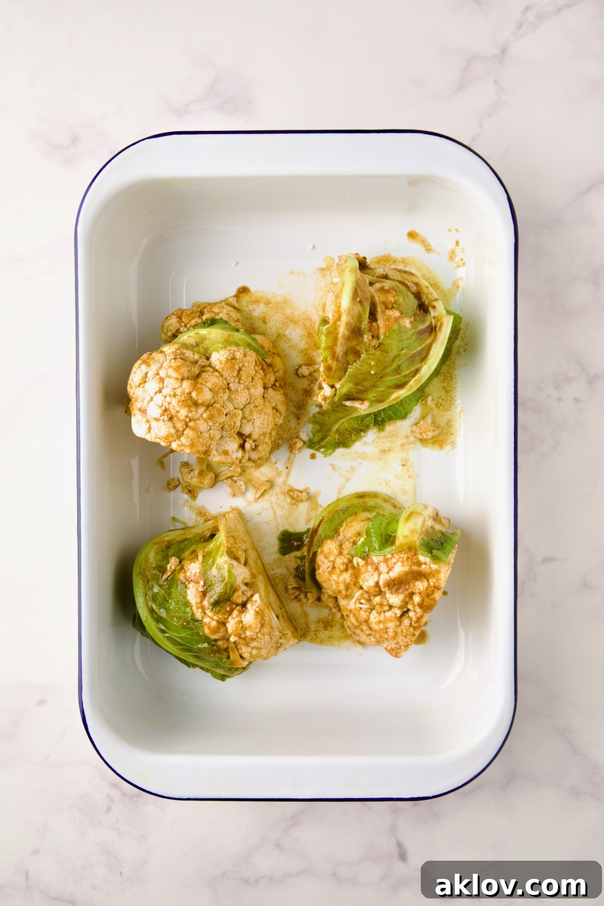 Four wedges of cauliflower in white roasting pan seasoned with curry powder before being roasted.