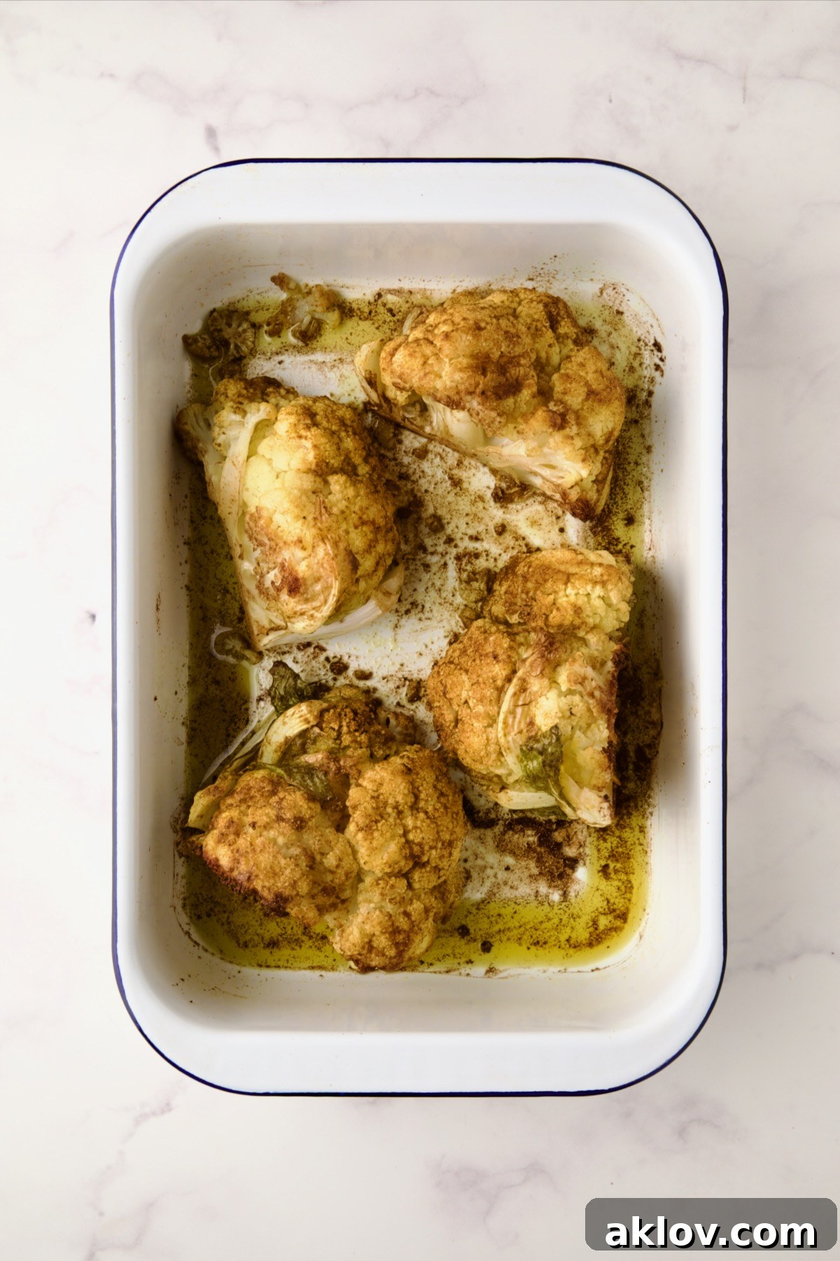 Four roasted wedges of cauliflower in white roasting pan.