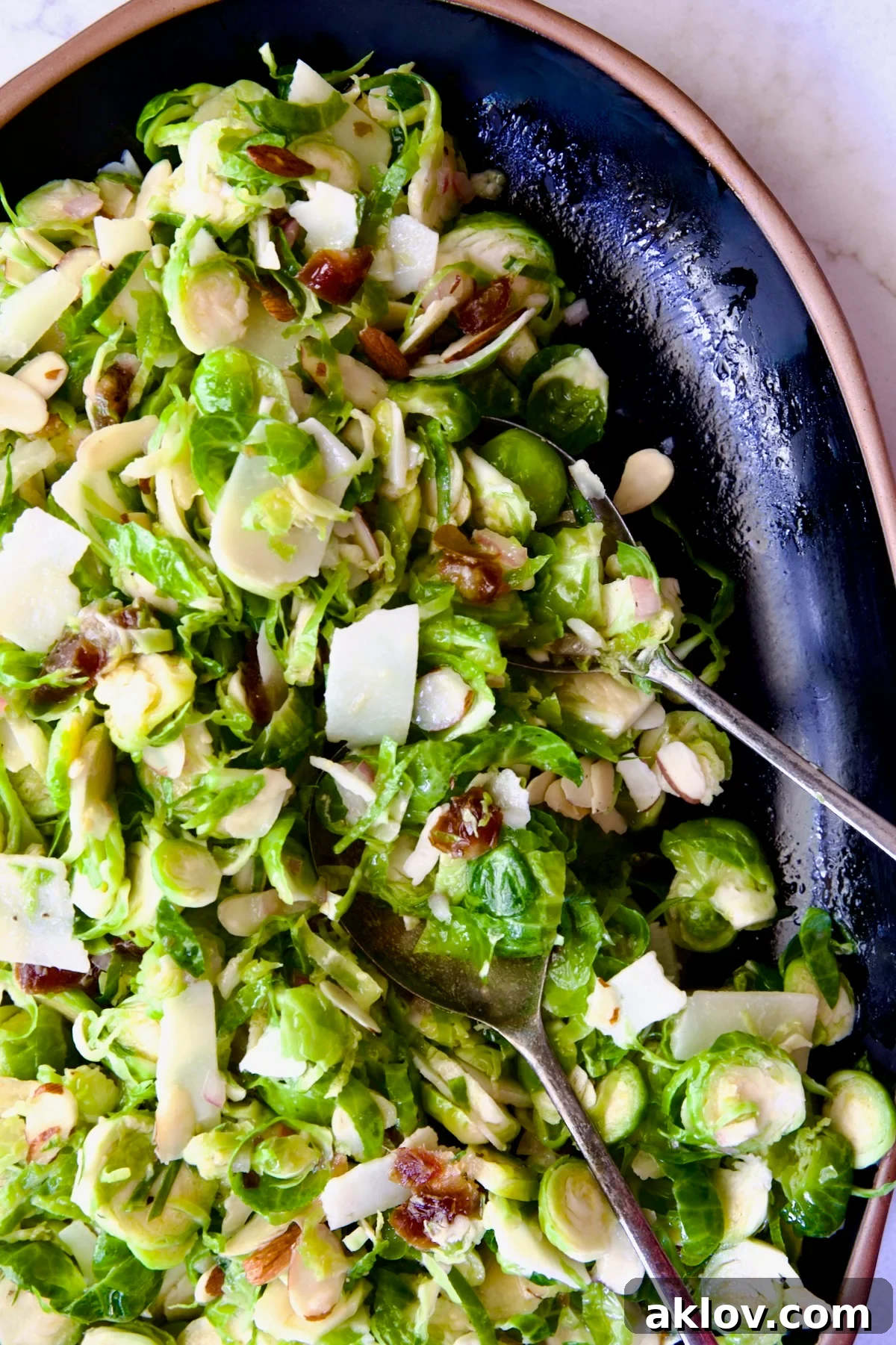 Zingy Shaved Brussels Salad 2 A beautifully presented Shaved Brussels Sprouts Salad on a black platter with a rustic brown rim, accompanied by elegant serving utensils, ready to be enjoyed.