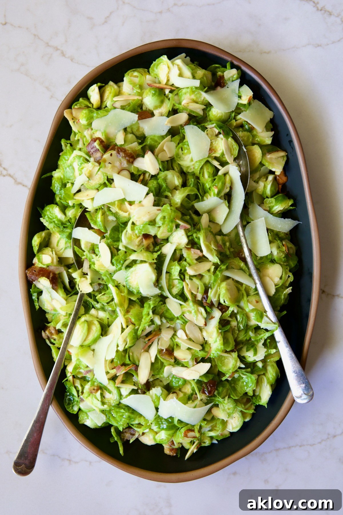 Zingy Shaved Brussels Salad 11 The prepared Shaved Brussels Sprouts Salad, elegantly arranged on a black platter with a warm brown rim, poised for serving with accompanying utensils.