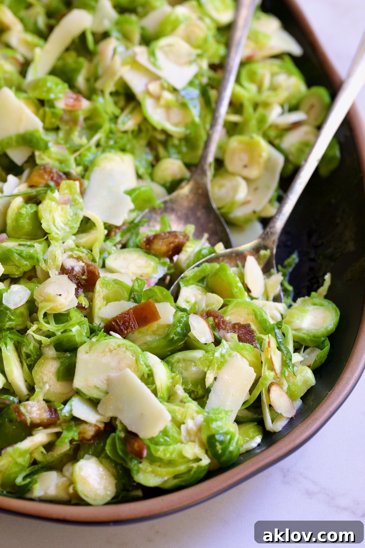 Zingy Shaved Brussels Salad 12 Serving utensils gracefully scooping a portion of Shaved Brussels Sprouts Salad from a black platter with a brown rim, showcasing the salad's readiness for enjoyment.