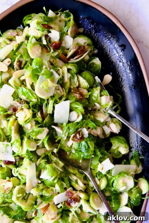 Zingy Shaved Brussels Salad 14 Shaved Brussels Sprouts Salad on black platter with brown rim and serving utensils.
