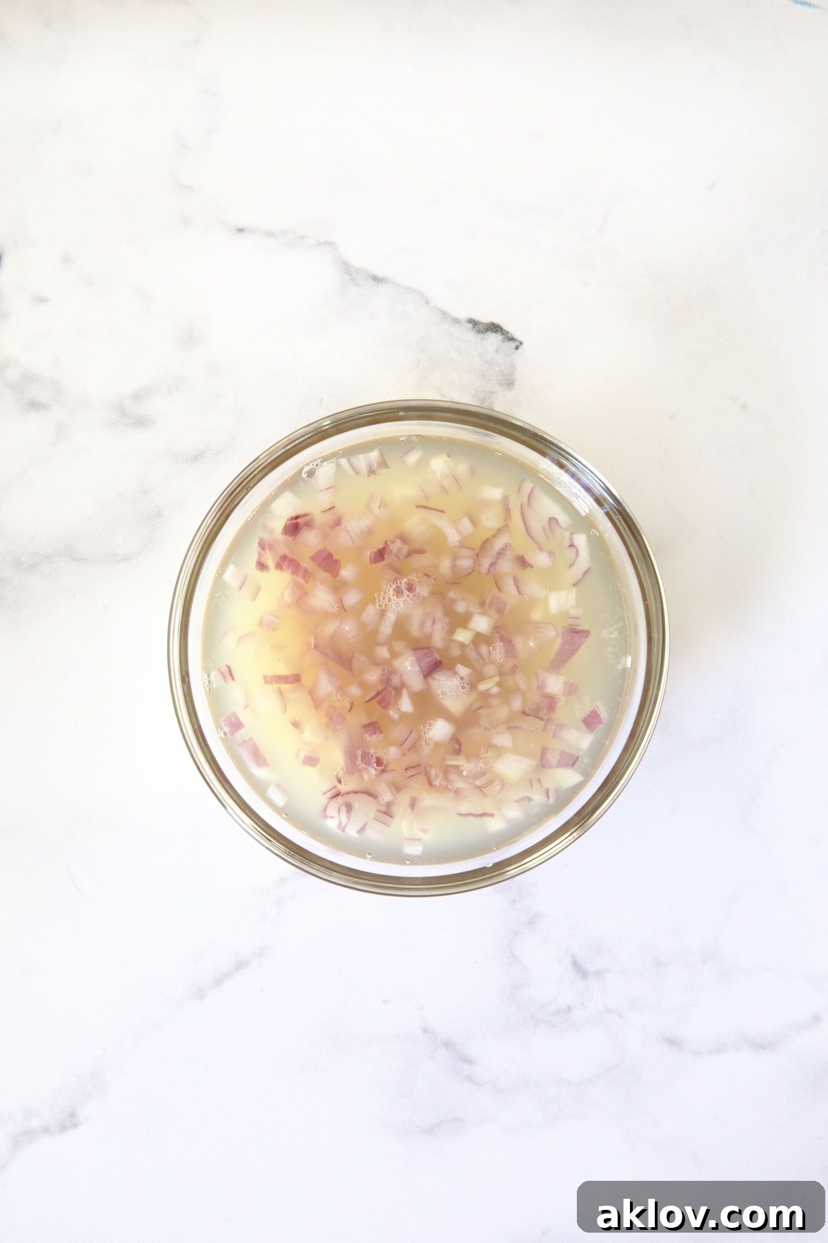 Zingy Shaved Brussels Salad 5 Finely chopped shallots steeping in fresh lemon juice within a small glass bowl, a vital step for softening and infusing flavor for the dressing.