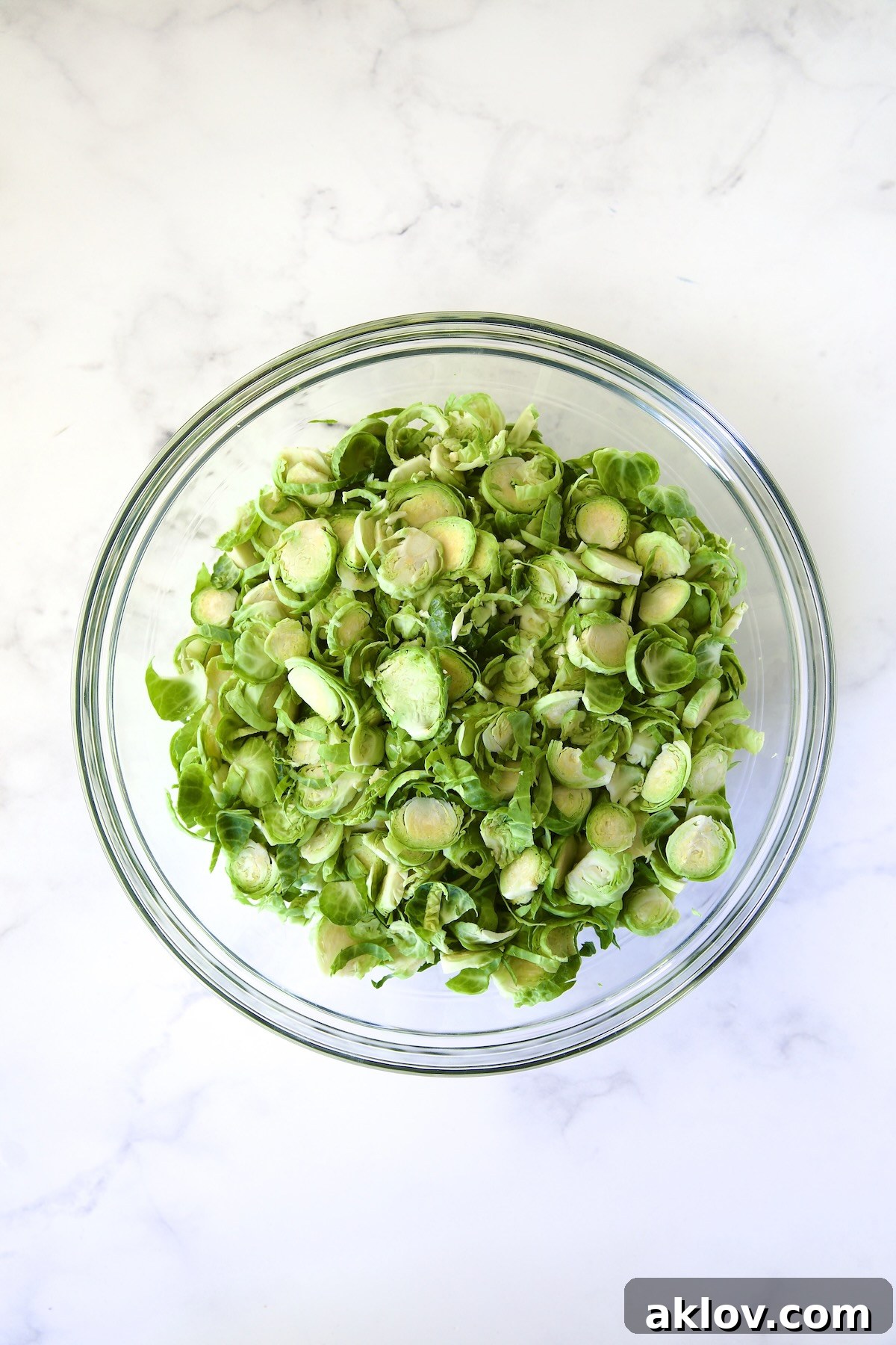 Zingy Shaved Brussels Salad 7 A generous quantity of thinly sliced (shaved) Brussels sprouts, gathered in a spacious glass bowl, forming the fresh base for the salad.