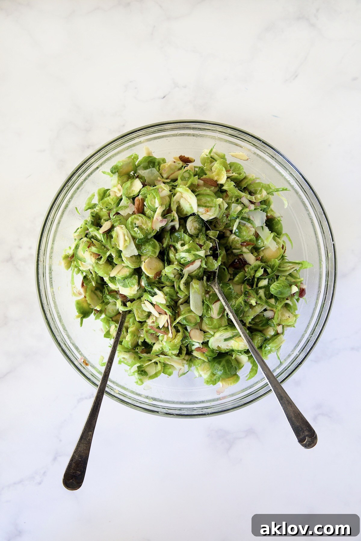Zingy Shaved Brussels Salad 10 The Shaved Brussels Sprouts Salad being meticulously mixed with the dressing in a large glass bowl, ensuring every ingredient is perfectly coated and infused with flavor.