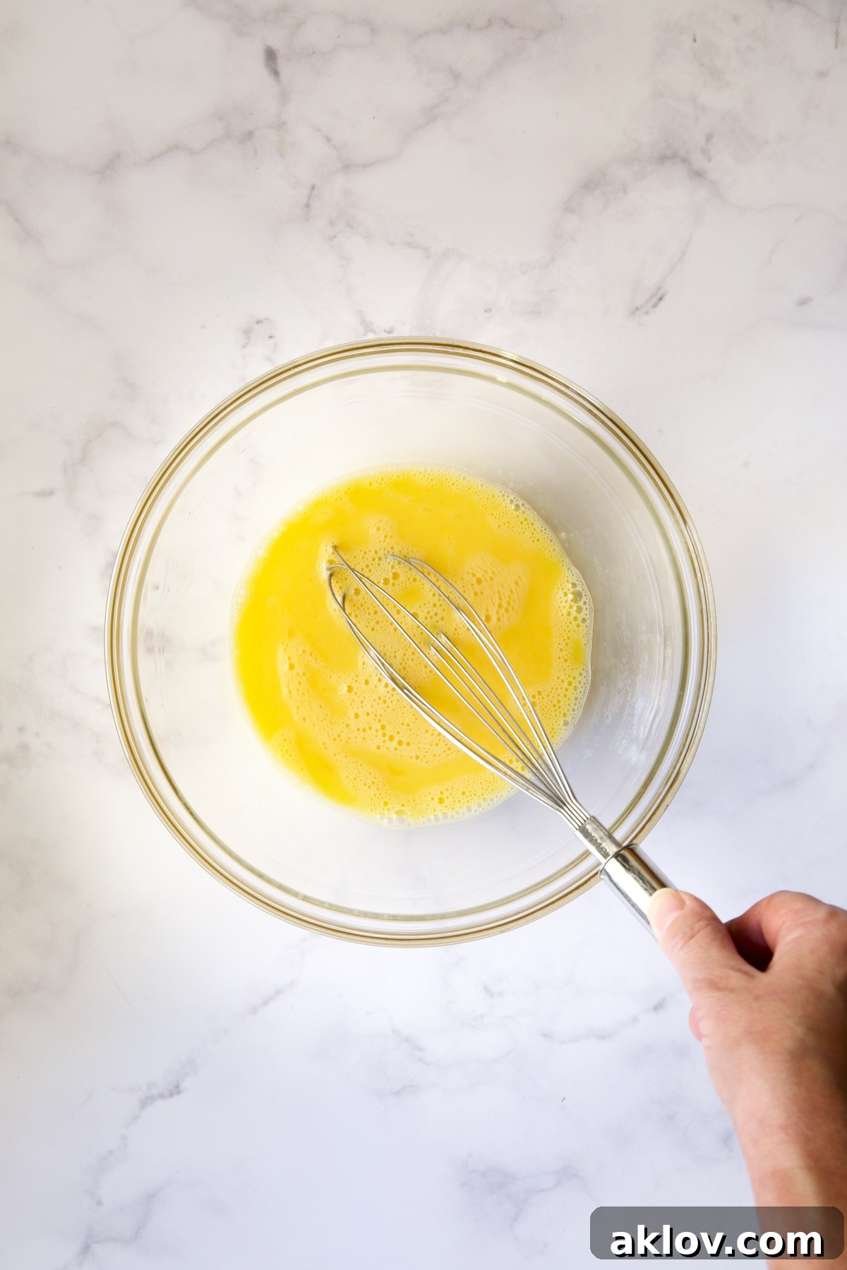 Eggs being beaten vigorously in a clear glass bowl, preparing for the soufflé mixture.