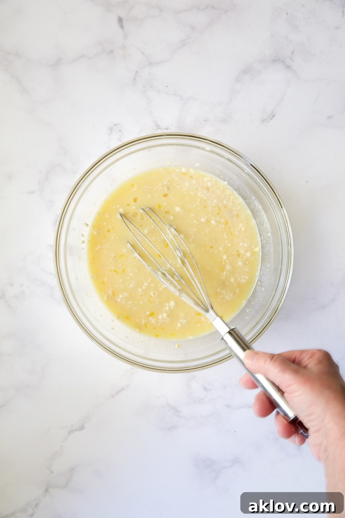 The whisked mixture of eggs, milk, flour, sugar, and extracts in a glass bowl, creating a smooth batter.