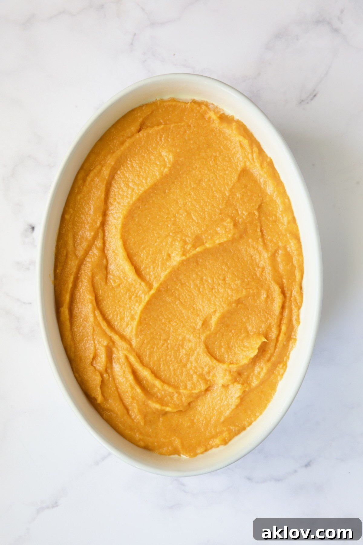 Sweet potato soufflé mixture in a white oval baking dish, before the streusel topping is added.