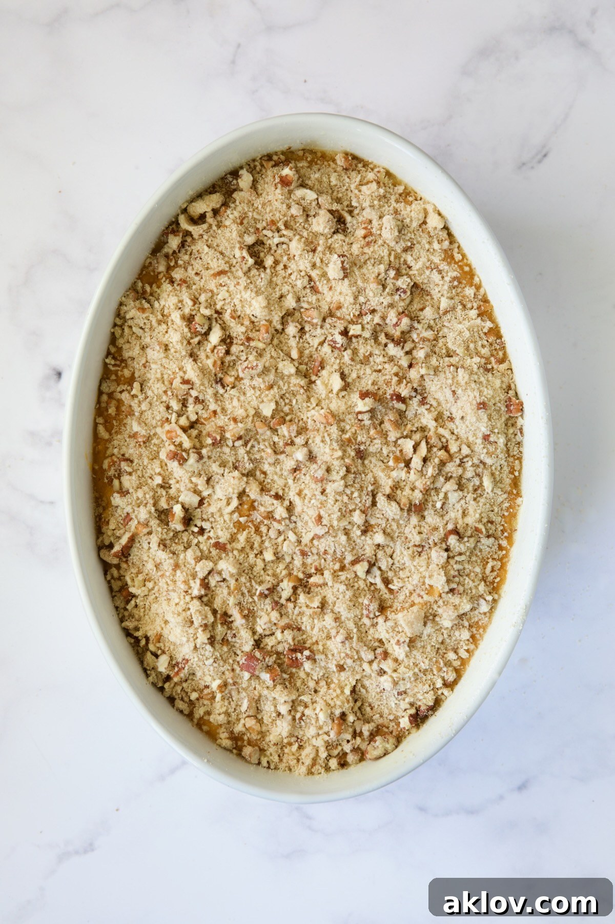 Sweet potato soufflé in a white oval baking dish, topped with pecan streusel, ready to be baked.