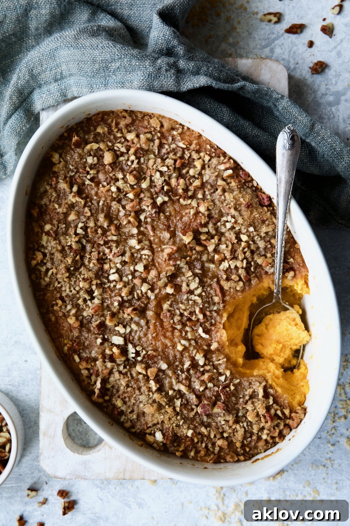 Sweet Potato Souffle in an oval baking dish, artfully arranged with blue napkin, scattered pecans, and brown sugar, highlighting its rustic elegance.