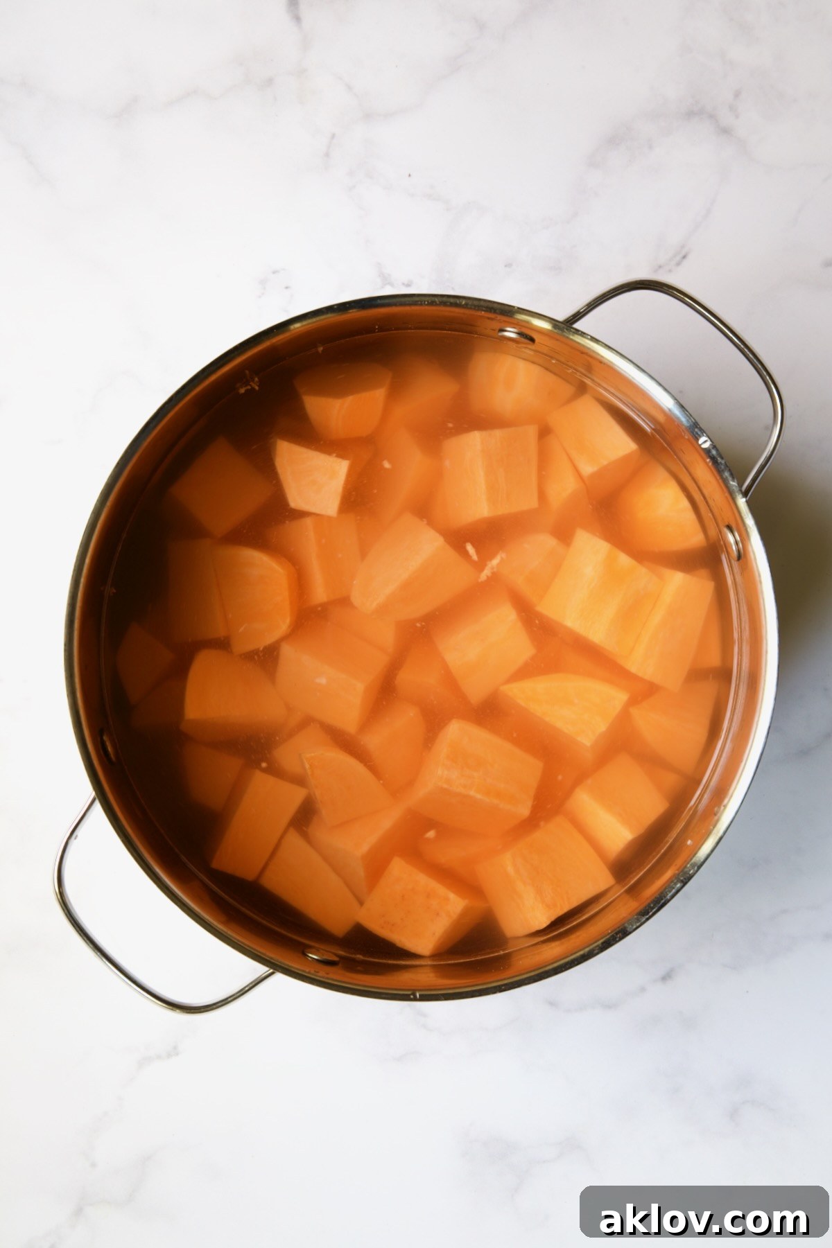 Uncooked sweet potatoes, peeled and cubed, in a stainless steel pot covered with water, ready for boiling.