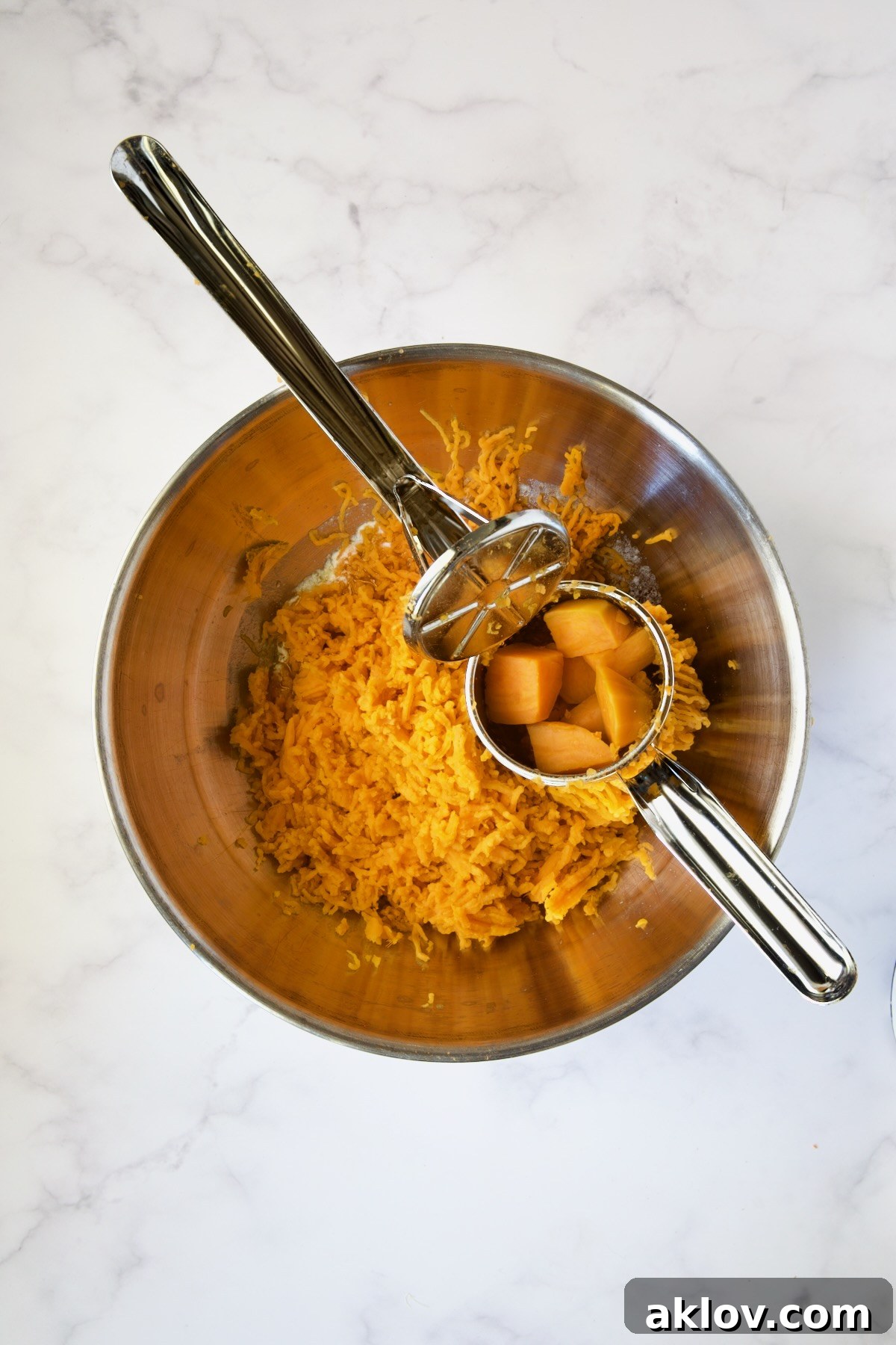 Hot sweet potatoes being processed through a ricer directly into a stainless steel bowl with melted butter.