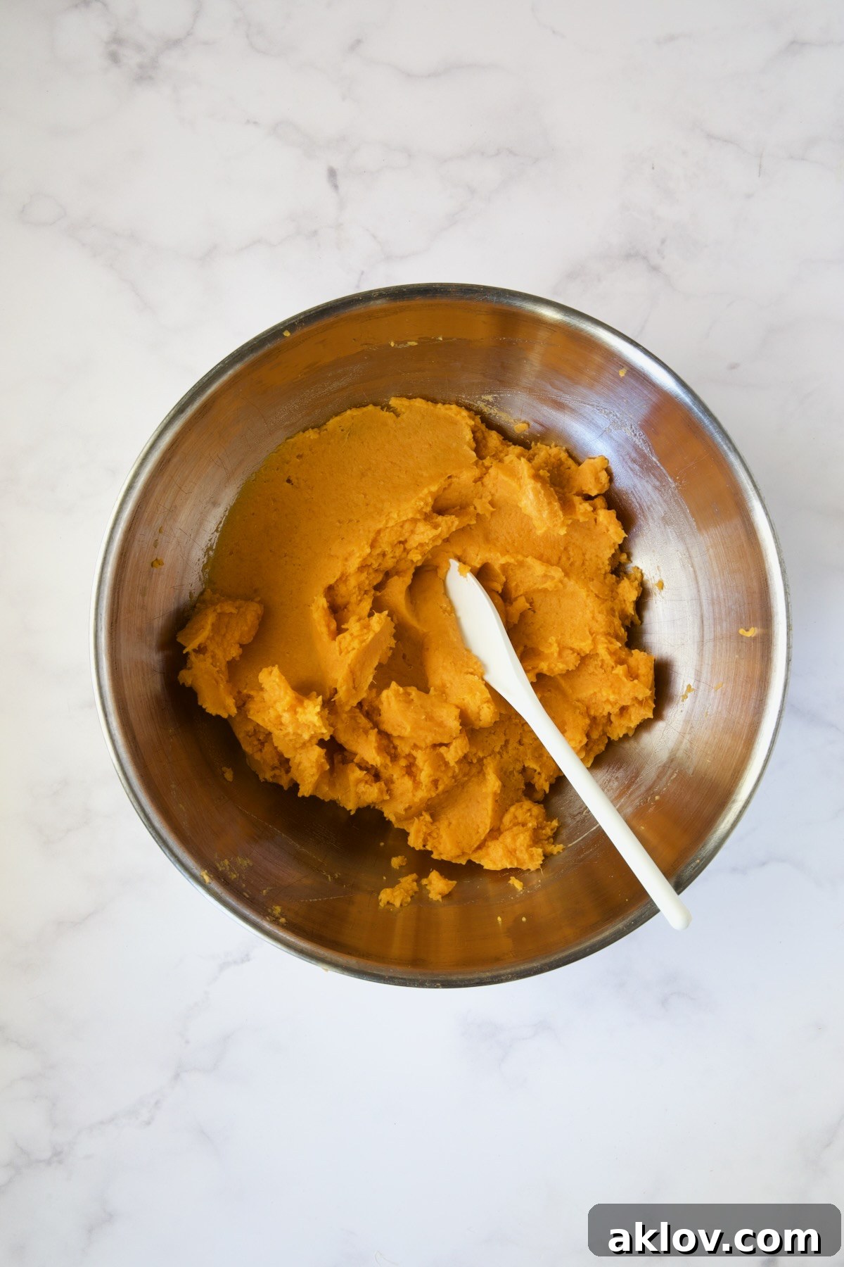 Smooth, mashed sweet potatoes mixed with butter in a stainless steel bowl.