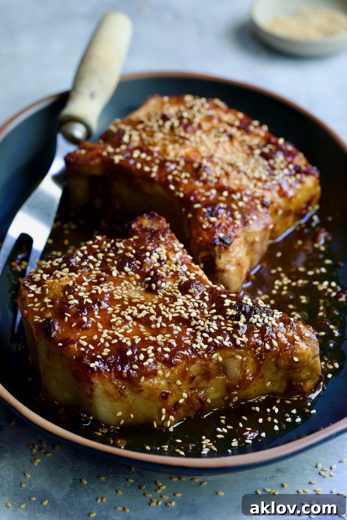 Two Asian Pork Chops on a black oval platter, generously garnished with sesame seeds, presenting a delicious meal.