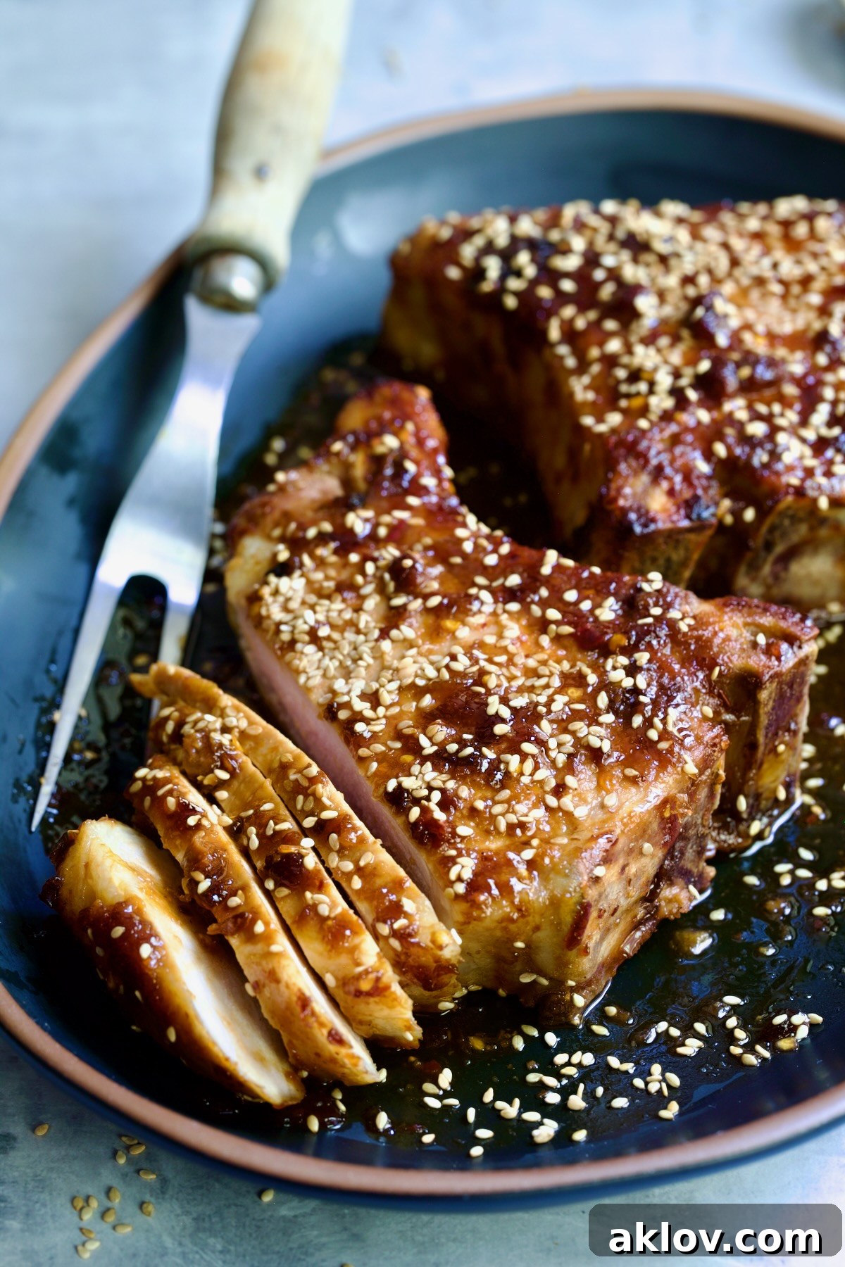 Two Asian Pork Chops on a black oval platter, garnished with sesame seeds, one partially sliced for serving.