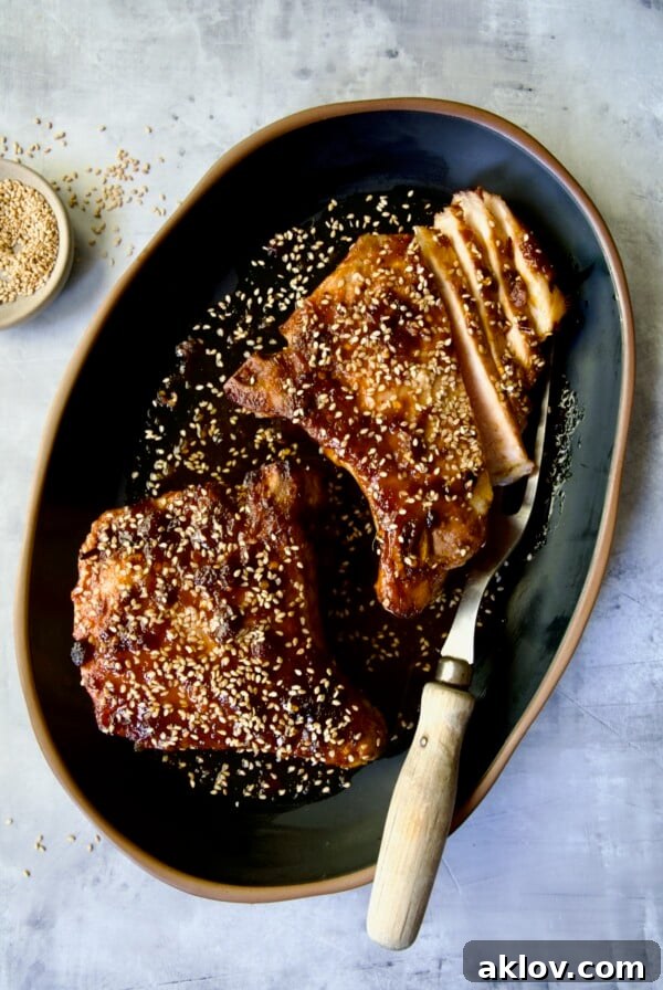 Two Asian Pork Chops on black oval platter garnished with sesame seeds with one pork chop partially sliced.