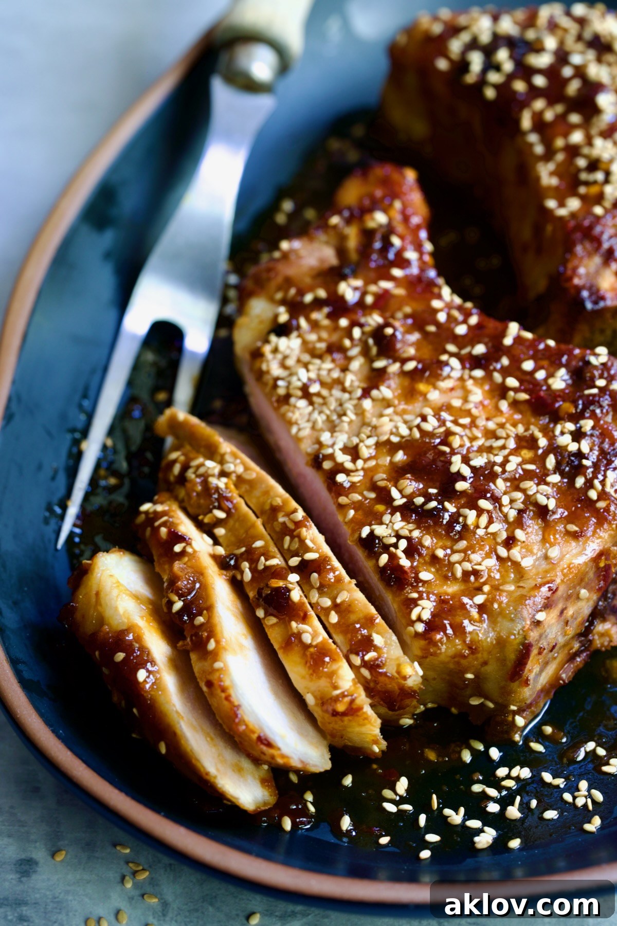 Partially sliced Asian Pork Chop on a black platter, garnished with vibrant sesame seeds, showcasing the tender meat.