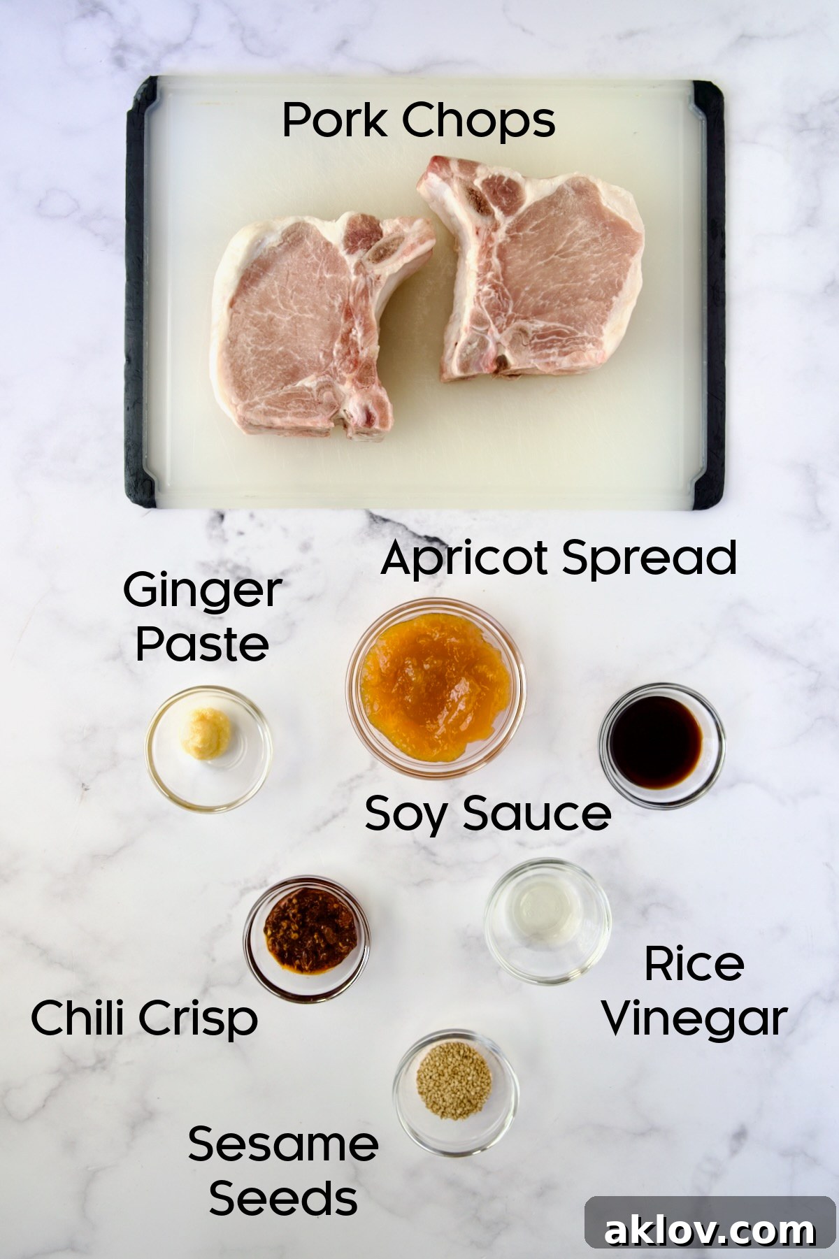 All ingredients for Asian Pork Chops neatly arranged in glass bowls, alongside two uncooked pork chops on a clean white cutting board.