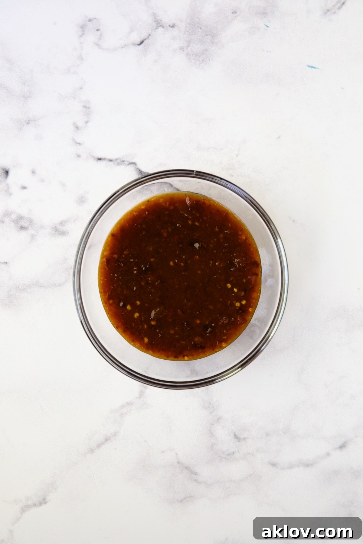 A glistening, rich glaze for pork chops, mixed in a clear glass bowl, ready to coat the meat.