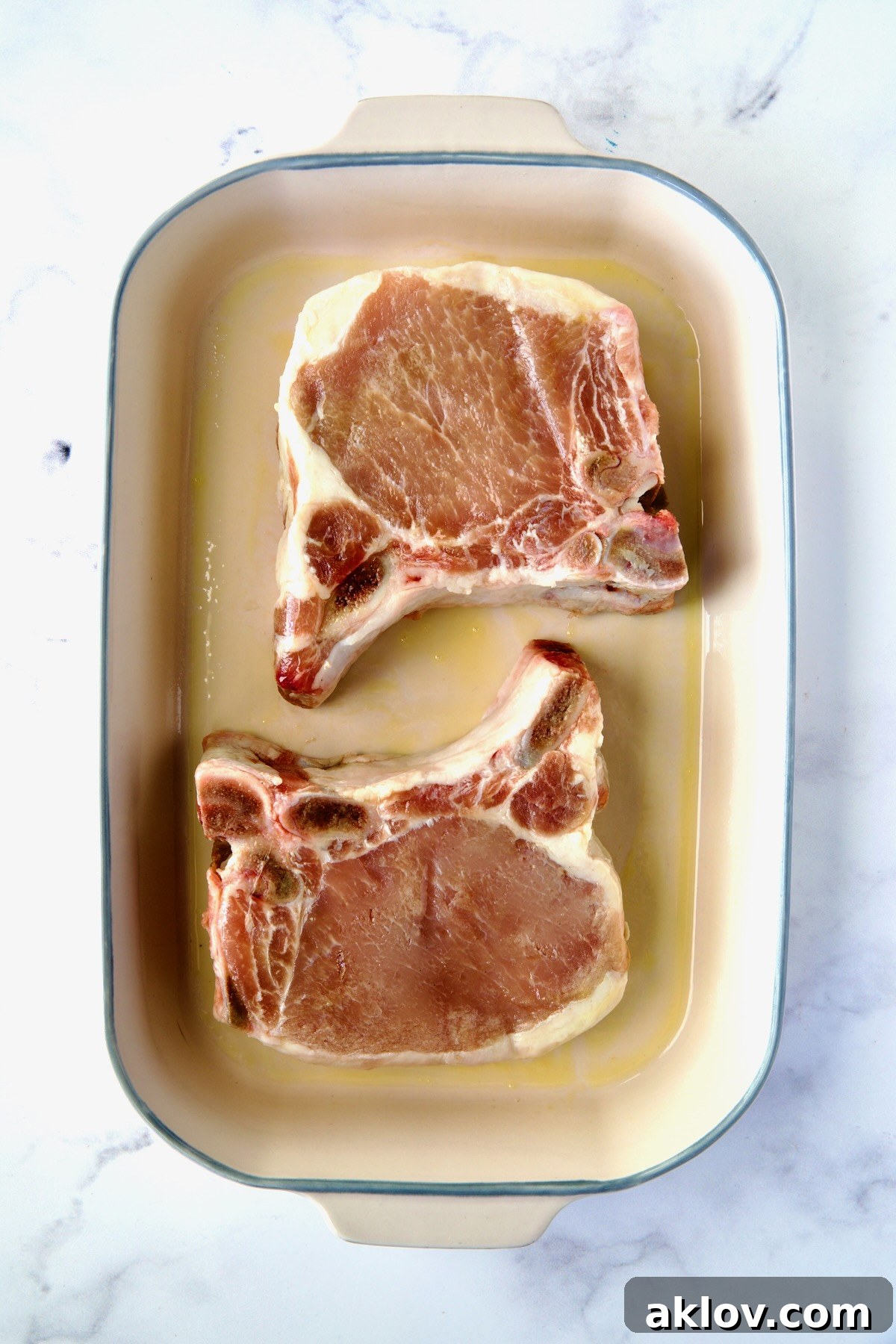 Two uncooked pork chops neatly arranged in a baking dish, awaiting their flavorful glaze.